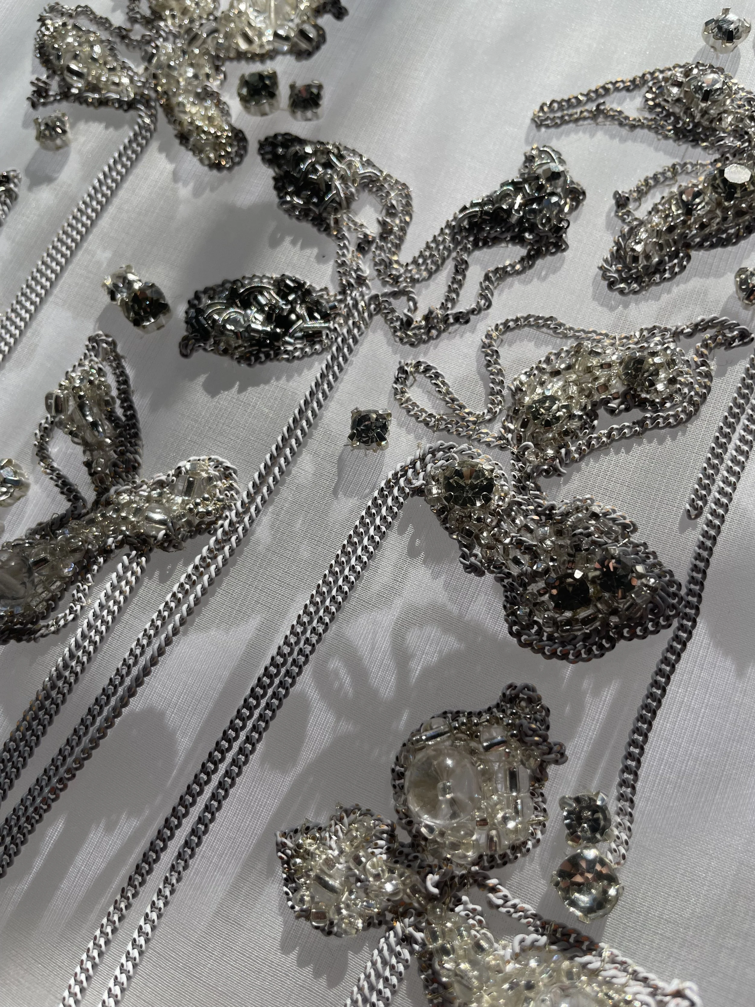 Close-up of silver and clear beaded jewelry, including chains and decorative pieces, laid out on a reflective surface.