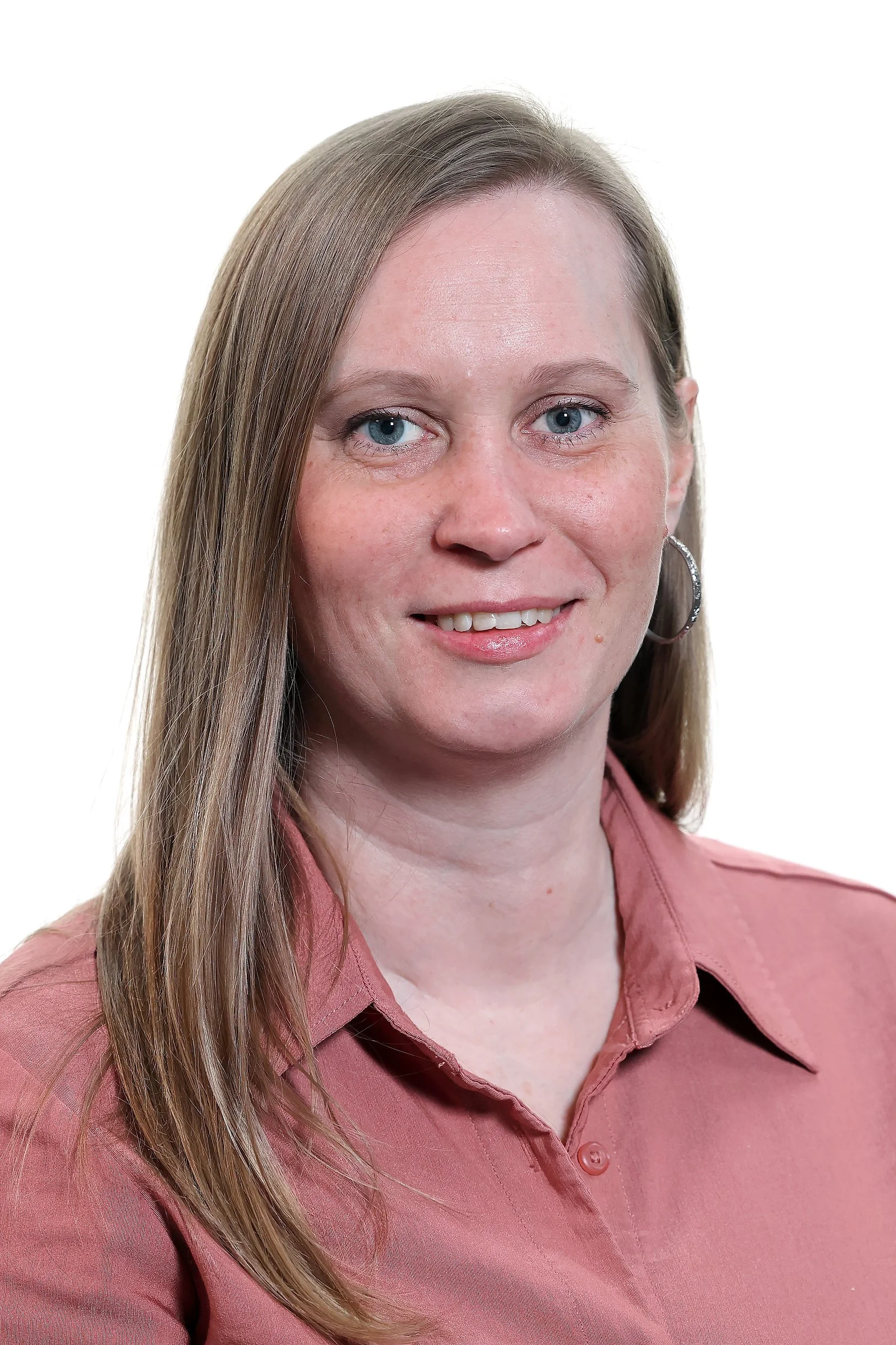Nærbilde av en kvinne med langt, lyst hår, blå øyne og eplefarga skjorte, smilende.