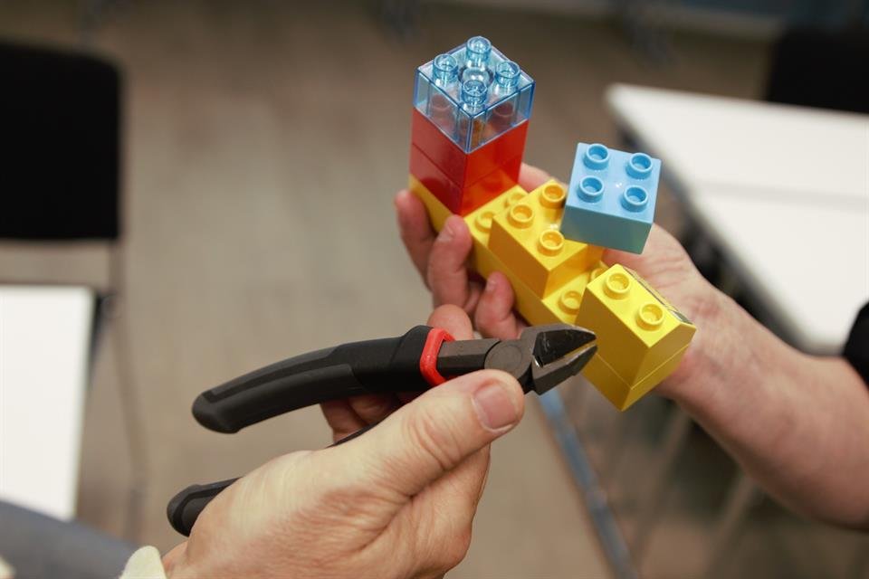 Hender holder LEGO-klosser og en liten verktøy med klippearmer.