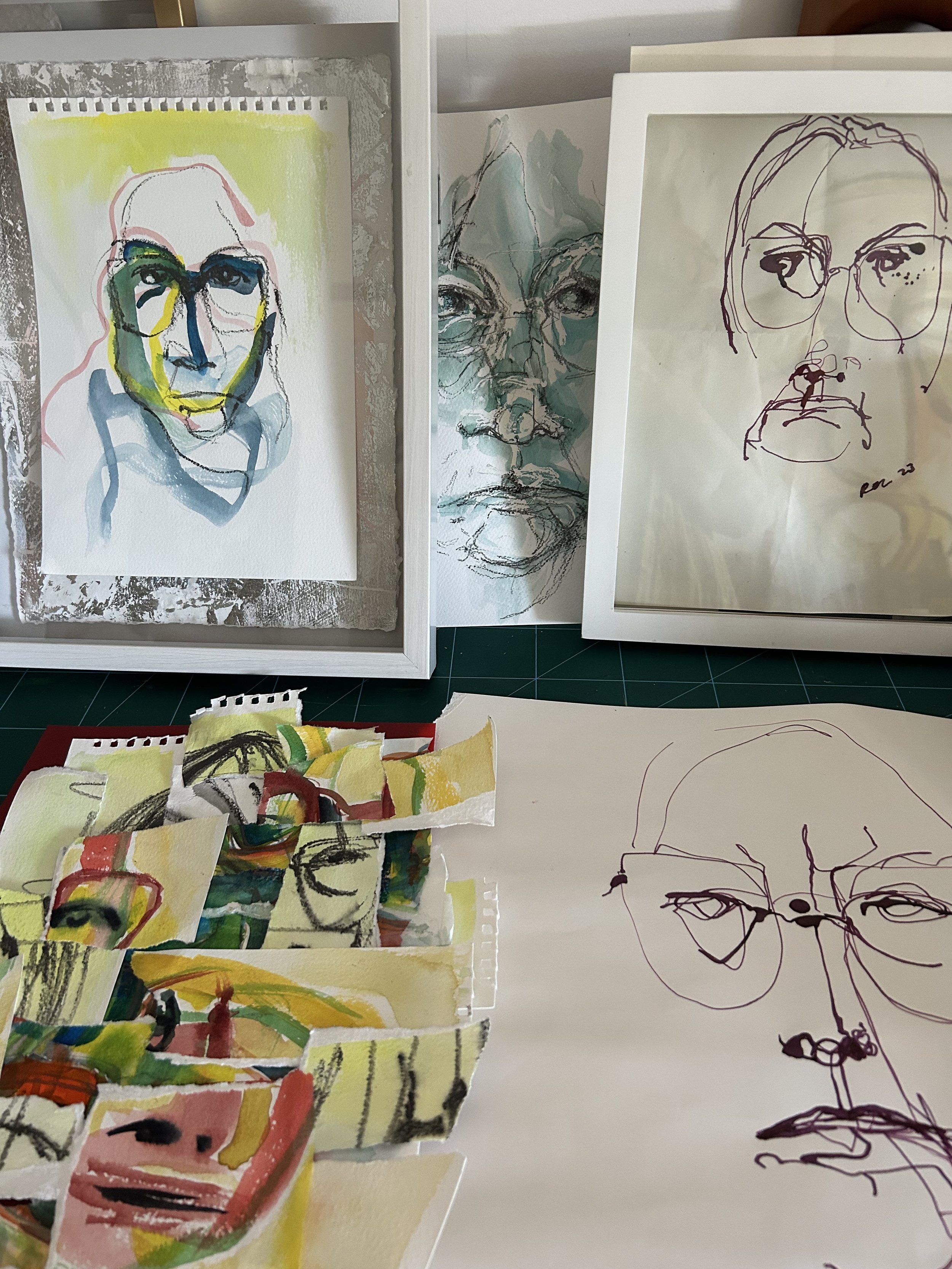 Roz Moreton self portrait drawings & paintings on paper, a detailed sketch of an her face, and minimalist line portraits of a her with glasses, displayed on white boards and scattered paper.