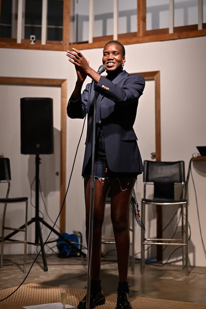 Nyaluak Leth smiling and clapping on stage in front of a microphone