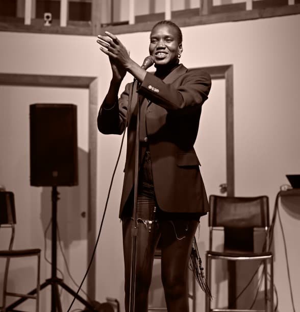 Nyaluak Leth smiling and clapping on stage in front of a microphone