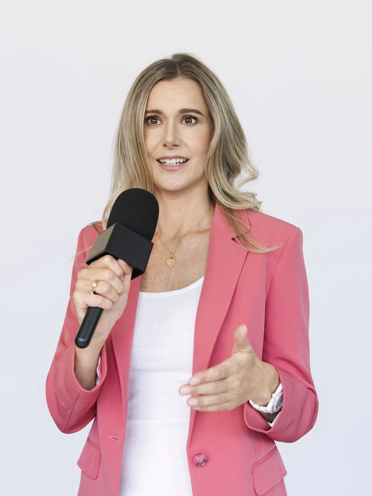Christina Voss spricht bei einer Präsentation über Burnout Präventation, hält ein Mikrofon in der Hand, trägt einen pinken Blazer und eine weiße Bluse.