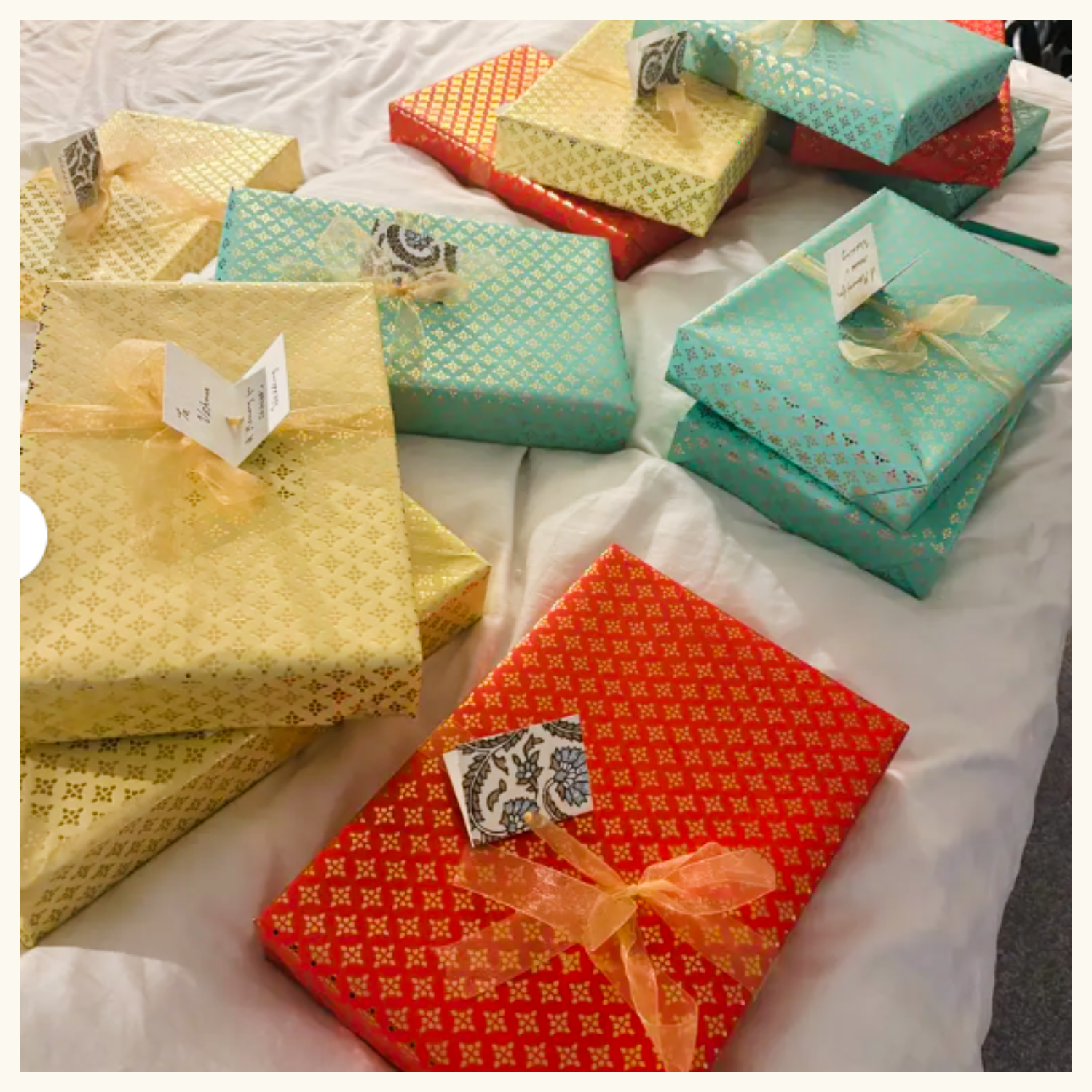 Multiple wrapped gift boxes in red, yellow, and turquoise with ribbon ties and decorative patterns, arranged on a white fabric surface.