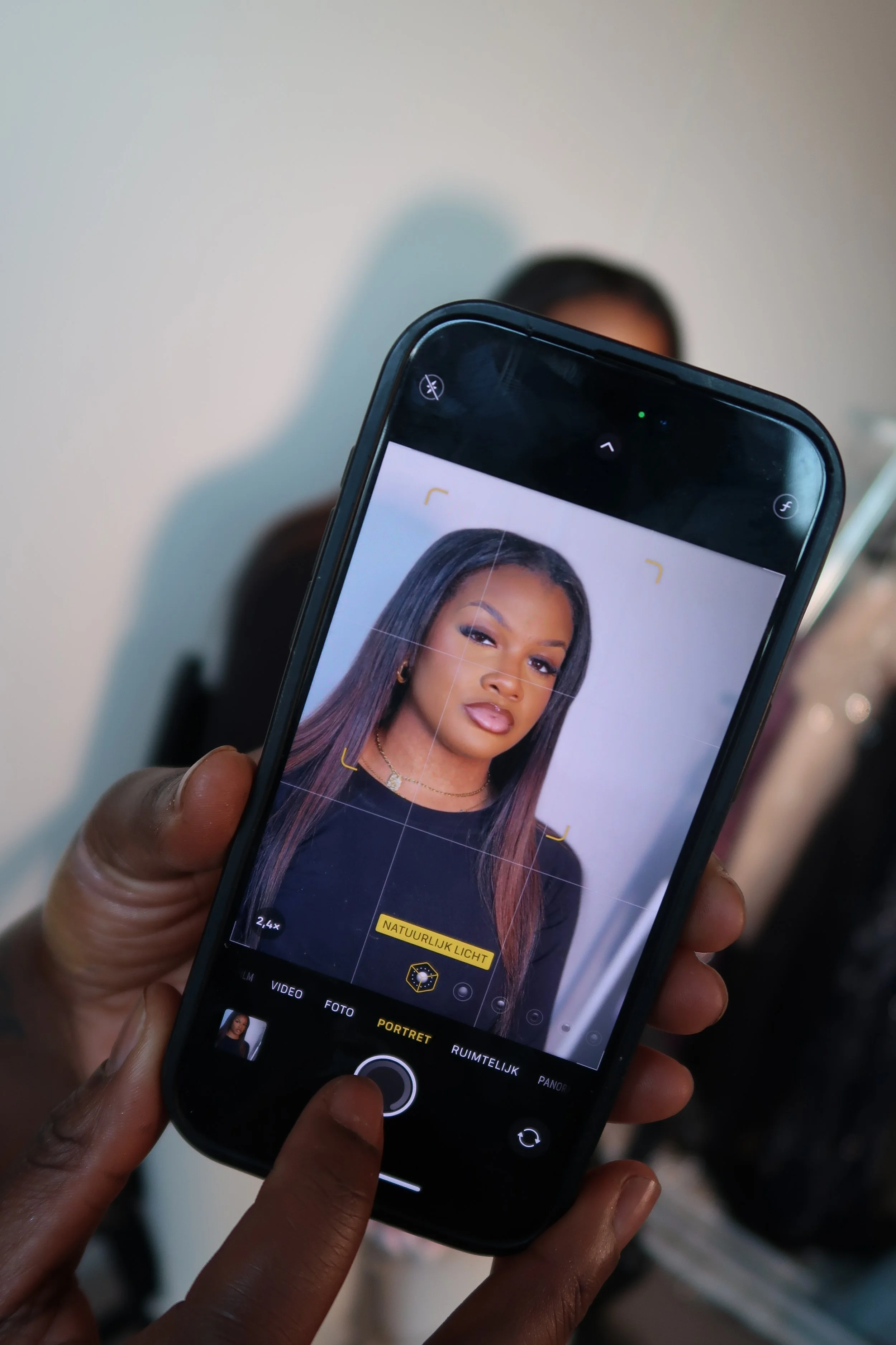 Close-up of a person holding a smartphone, camera app open, displaying a portrait of a woman with long hair, makeup, and jewelry.
