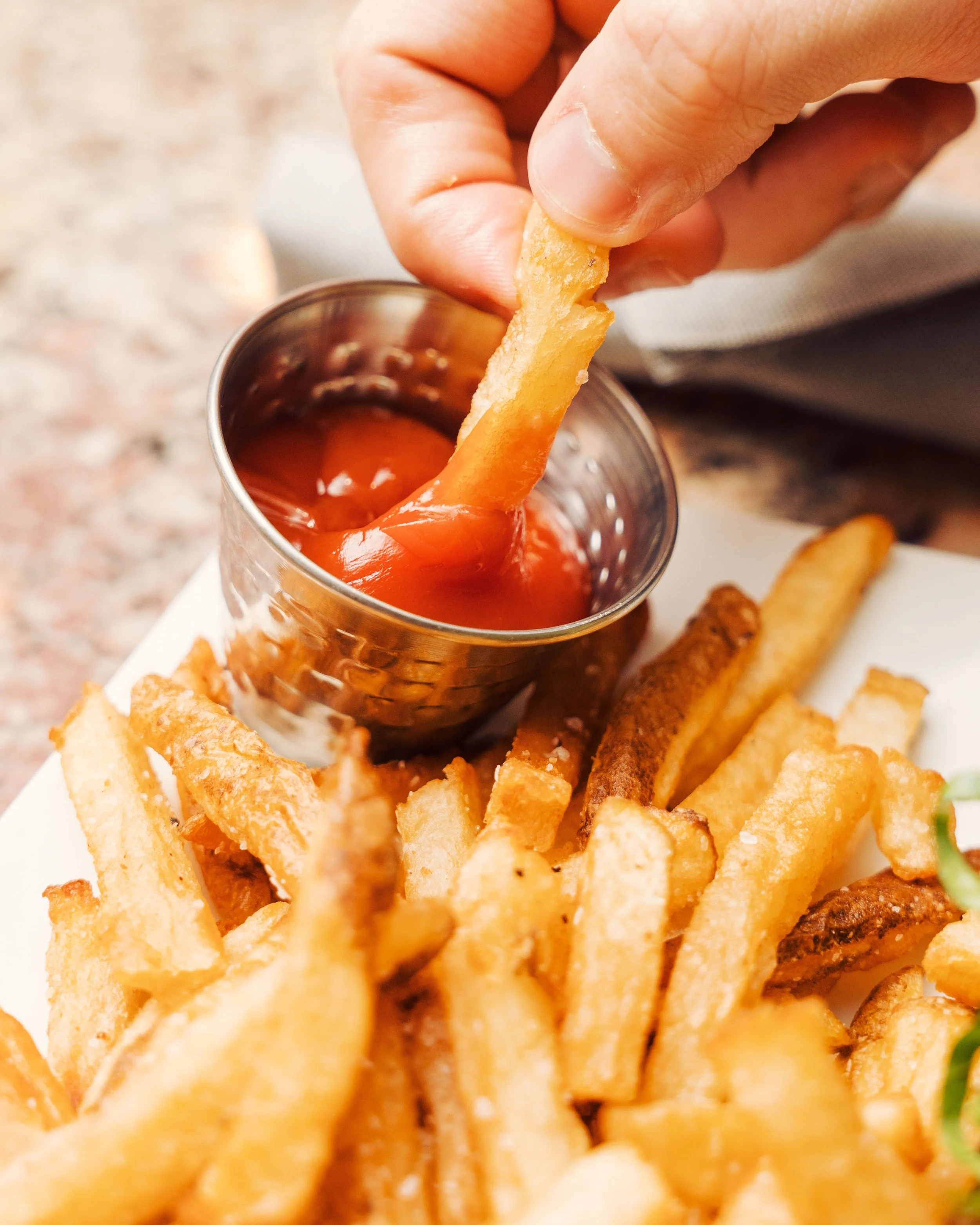 Gros plan sur une frite trempée dans du ketchup, entourée de frites croustillantes.