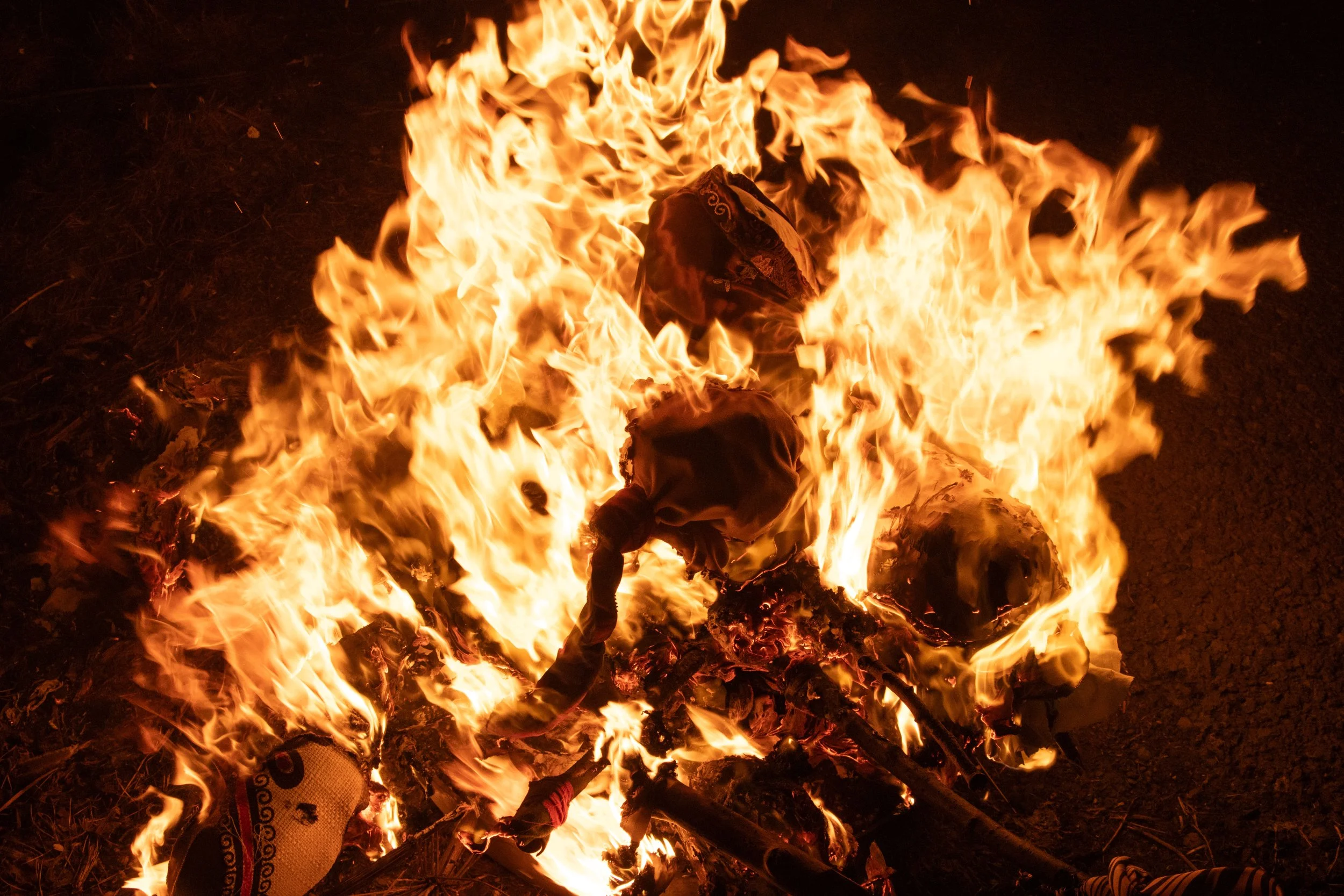 A large fire burning with orange and yellow flames, consuming wood and other materials on the ground in darkness. Marzanna. Morana