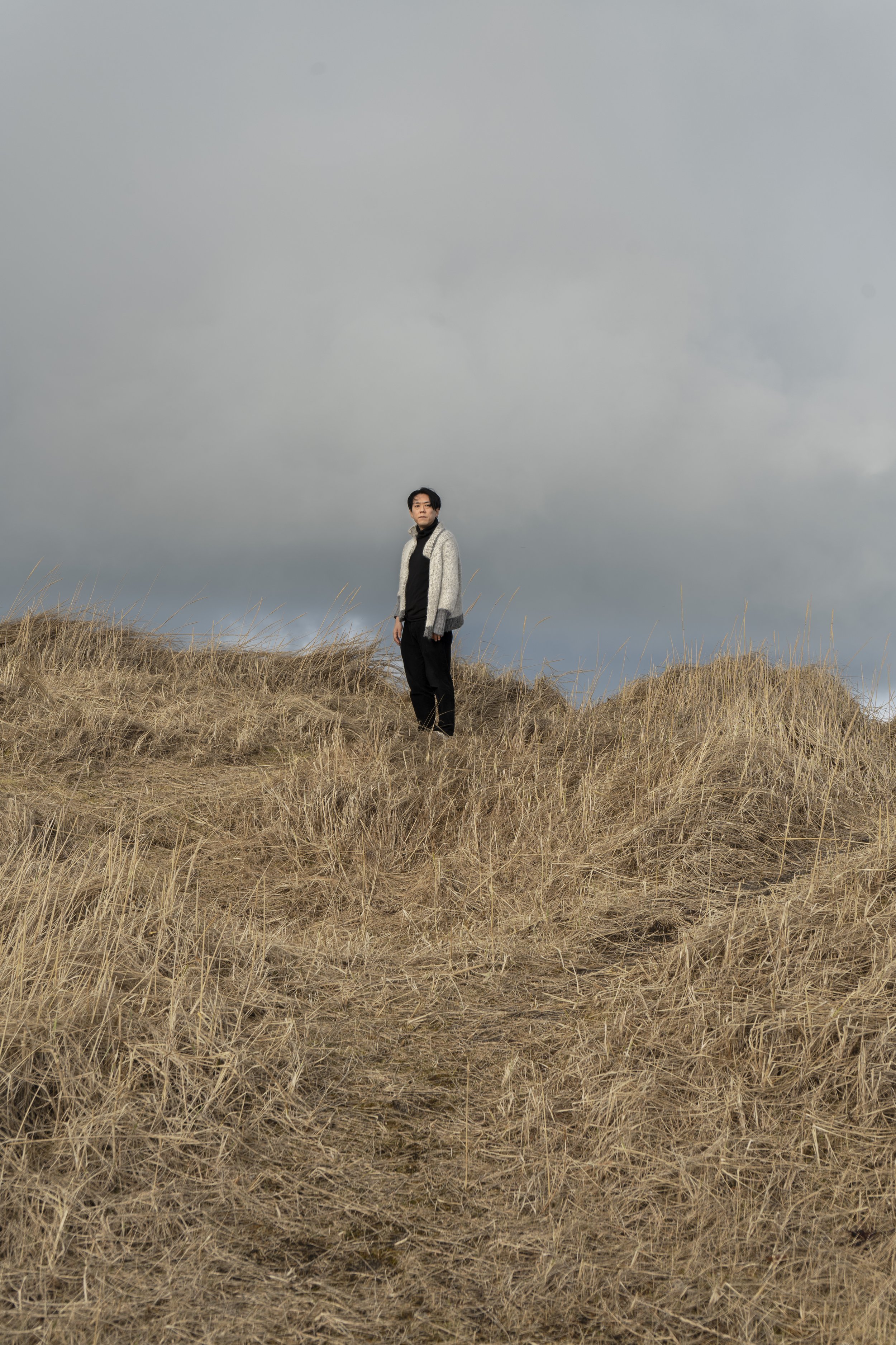 A person standing on a grassy hillside under a cloudy sky.