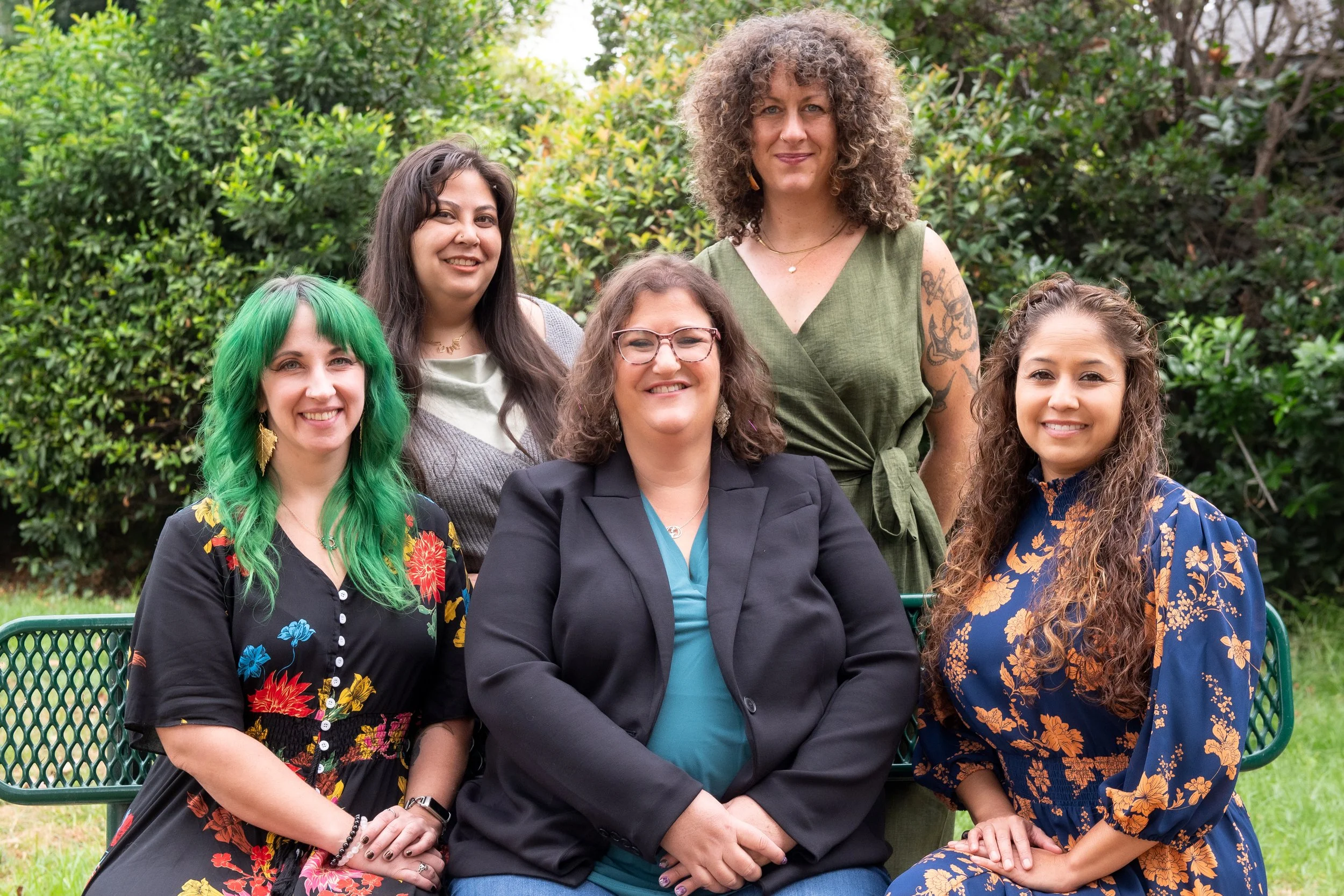 5 women are together outside. They are wearing formal outfits and all are smiling