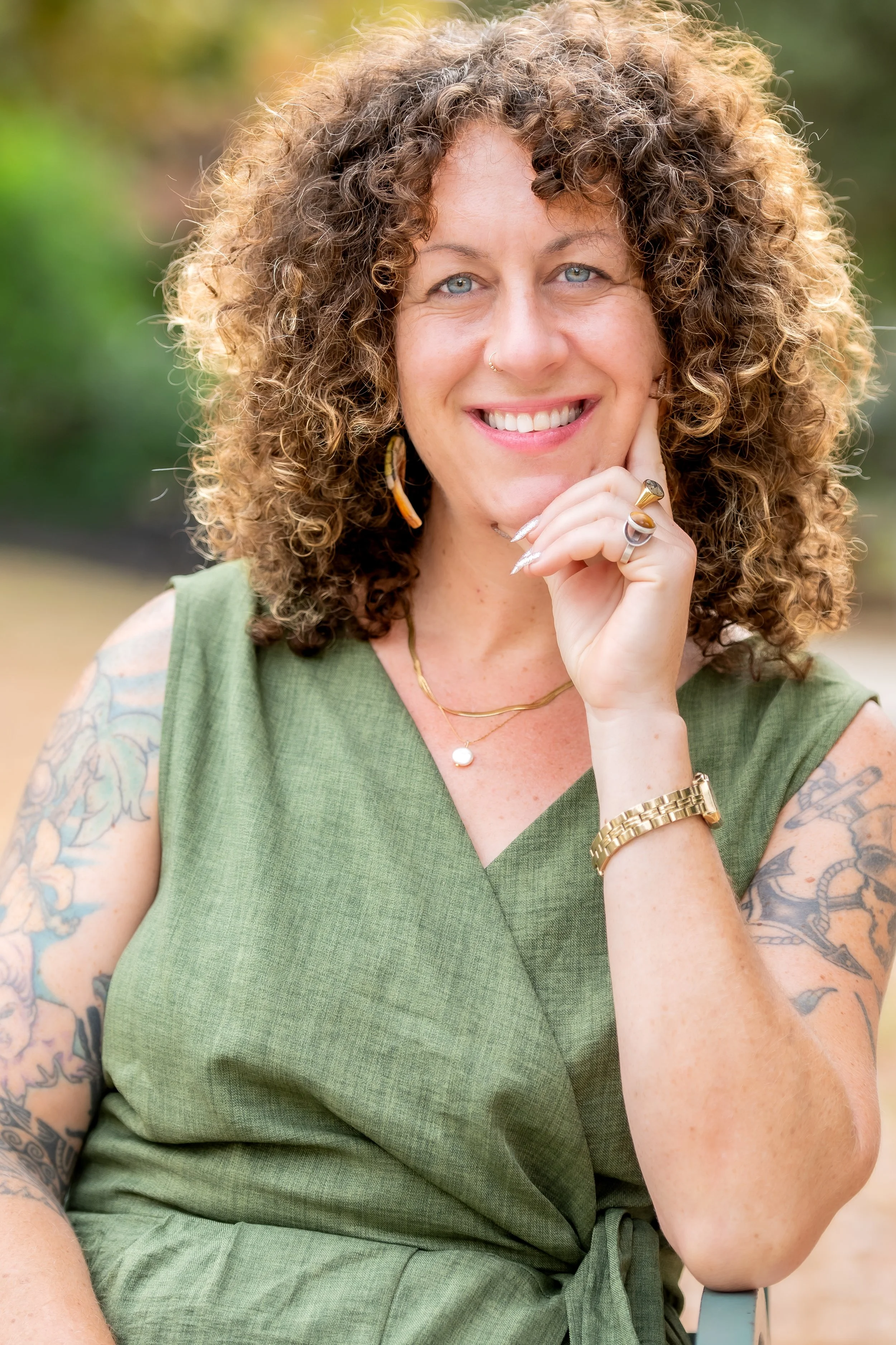 White woman with brown curly hair wearing a green outfit and smiling