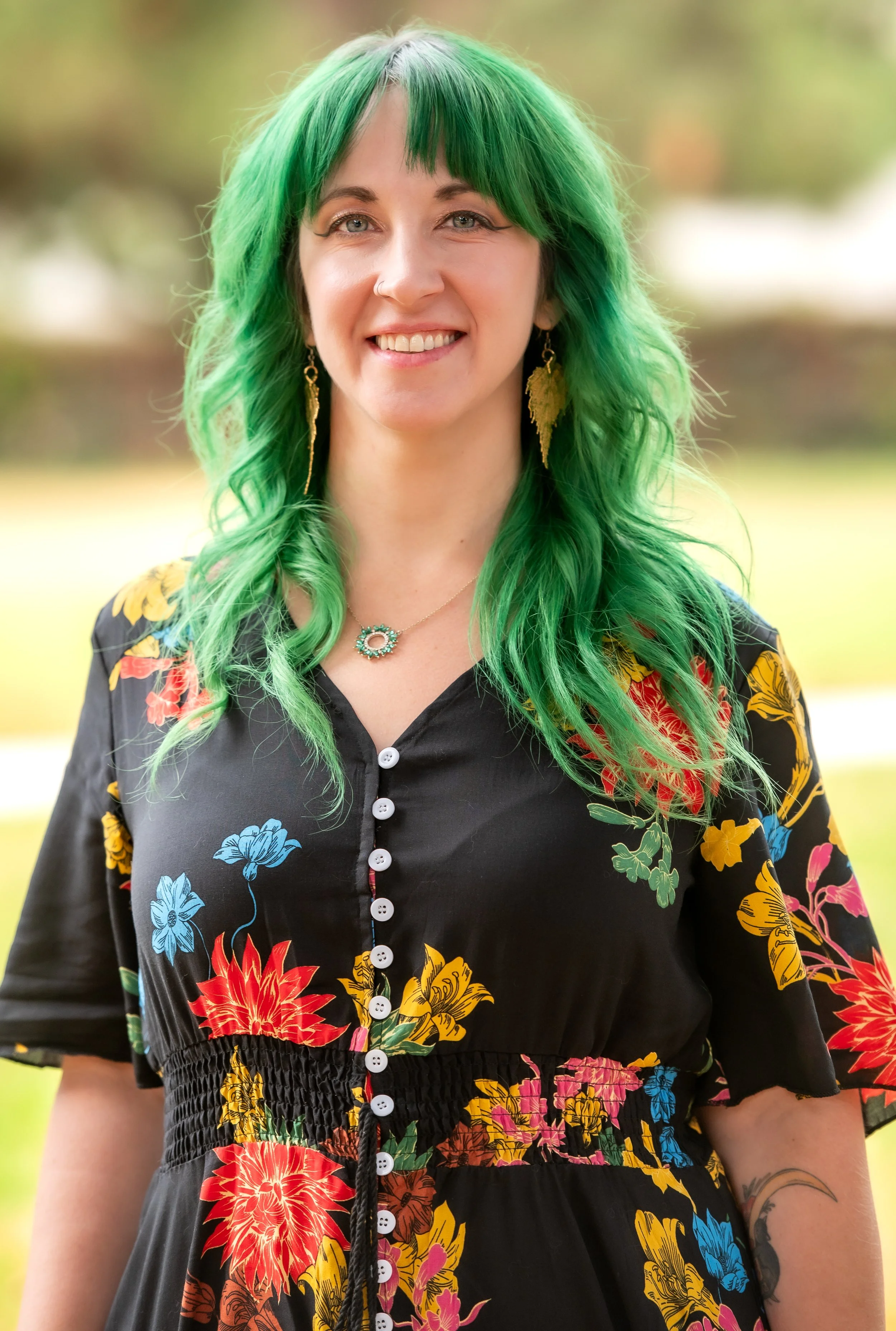 White woman with green hair. She is smiling and wearing a dress with flowers on it