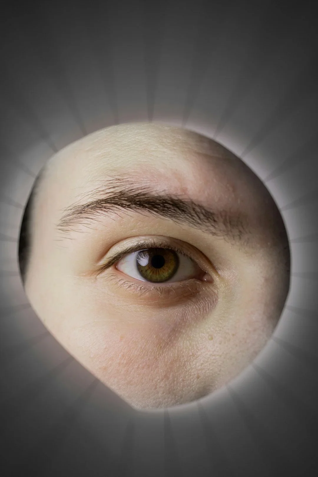Close-up of a human eye seen through a circular opening, with textured skin around the eye and radiating lines around the circle.