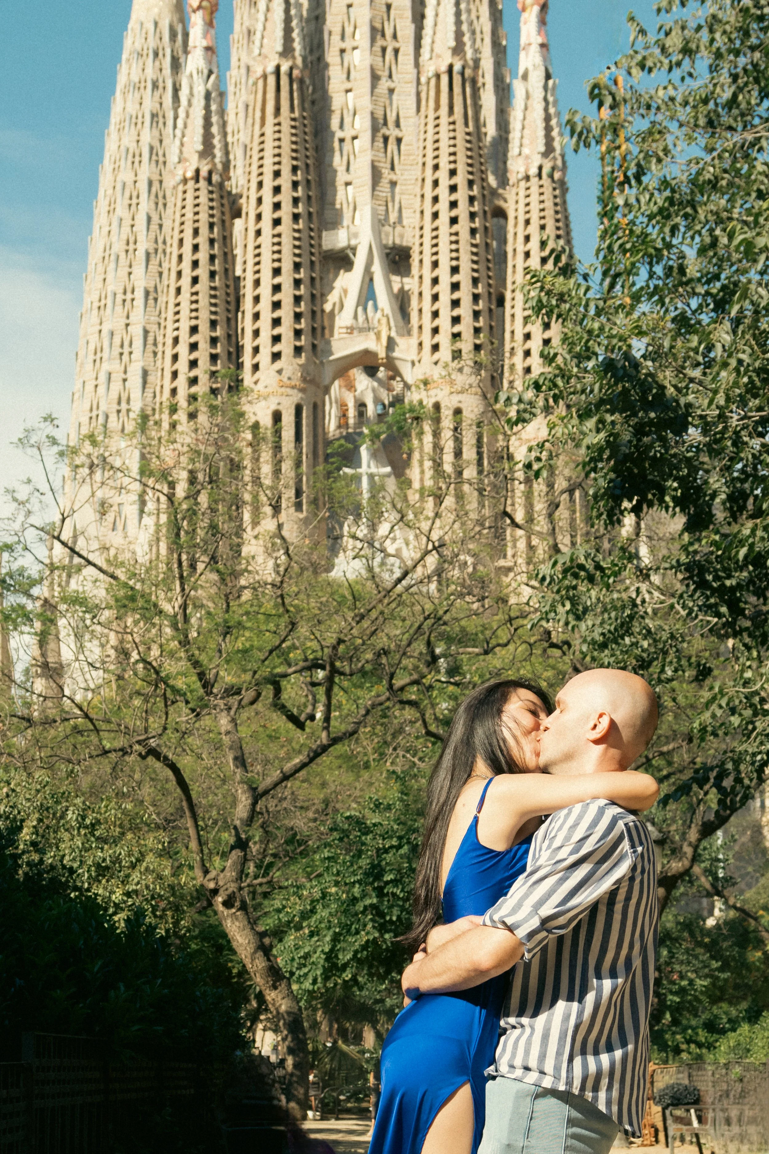 A couple kissing outdoors with the Sagrada Familia in the background in Barcelona, Spain.