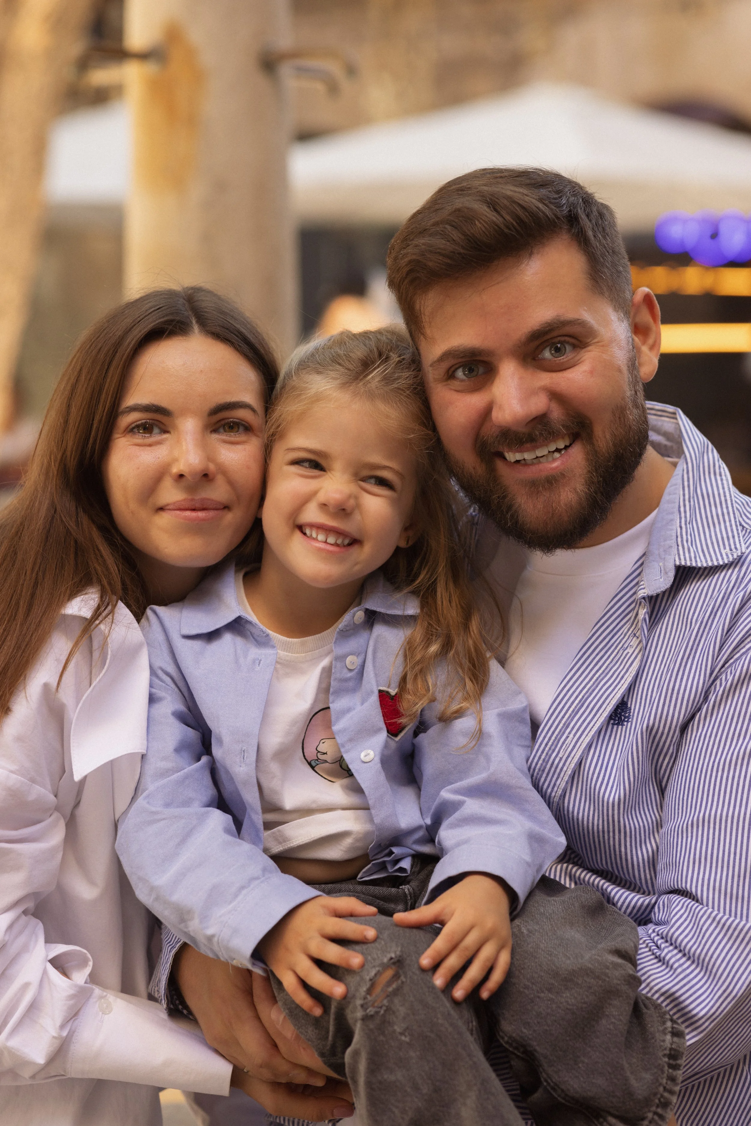 Happy family of three, a woman, a young girl, and a man, smiling for the camera in an outdoor setting.