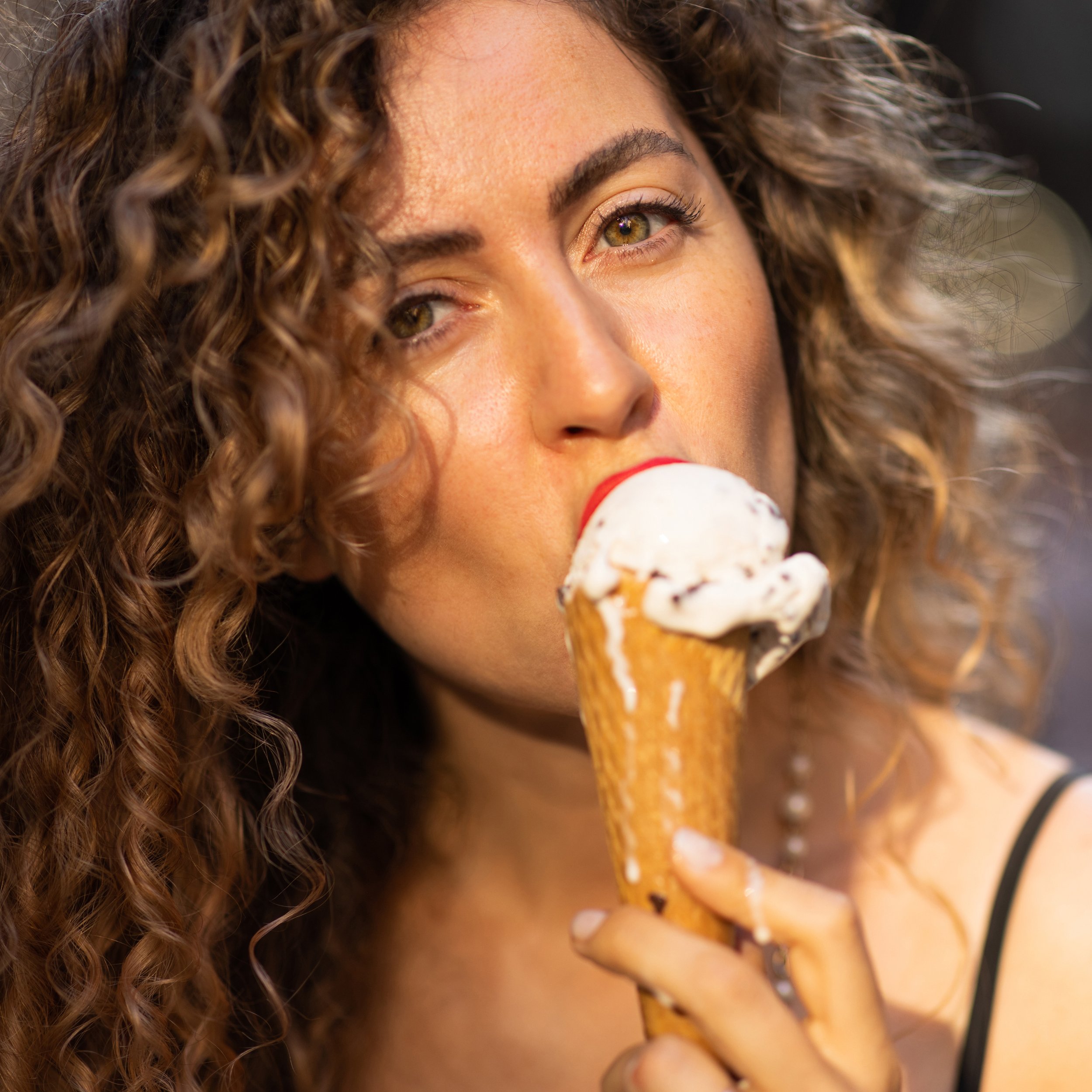 Woman with curly hair and light makeup eating an ice cream cone