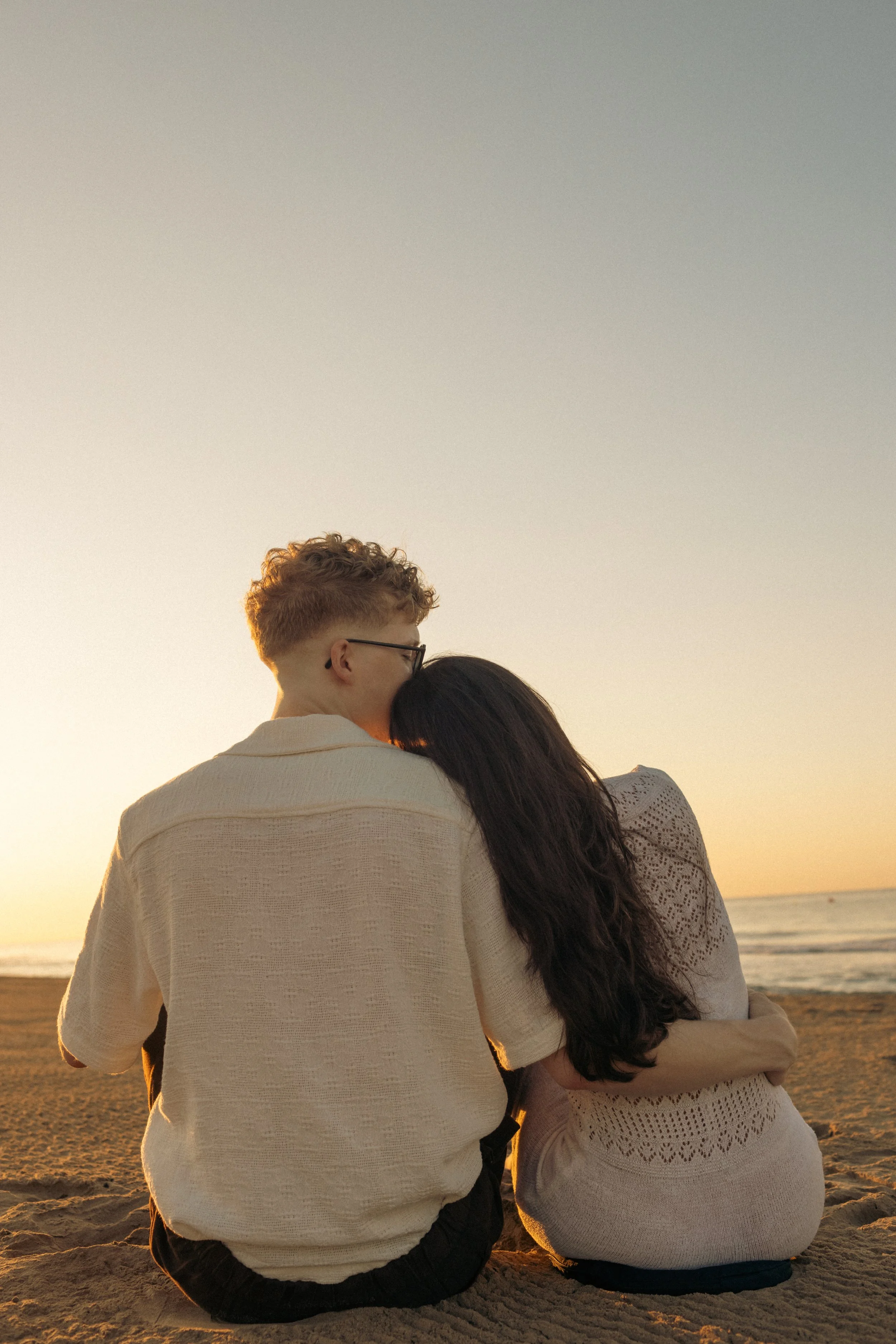 A couple sitting on the beach at sunset, embracing and sharing a tender moment.
