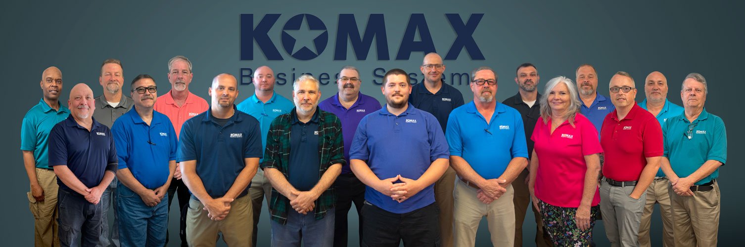 Group of 17 people standing in front of a wall with the KOMAX Business System logo.