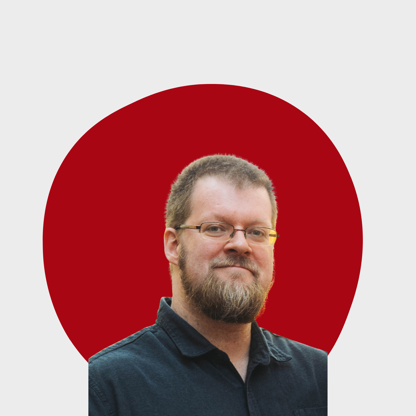 Portrait of a man with glasses, a beard, and short hair, wearing a dark shirt, in front of a red circular background.