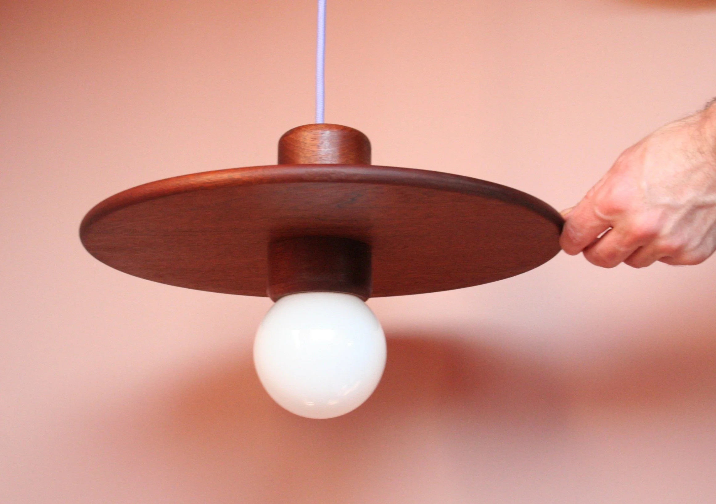 Een hand houdt een cirkelvormige plafondlamp met een houten rand en een witte bol in het midden.