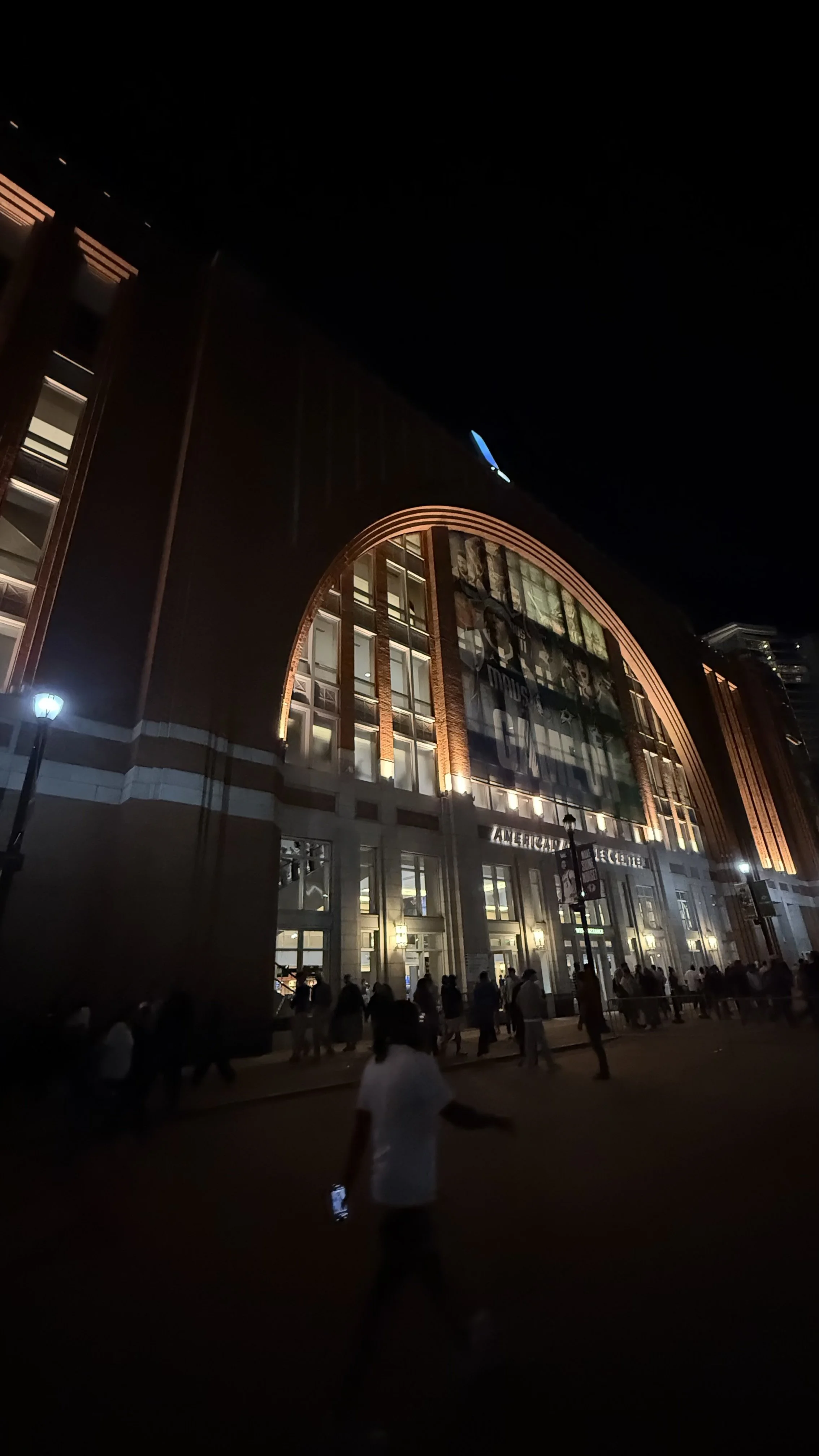 Exterior of American Airlines Center at night with people walking.
