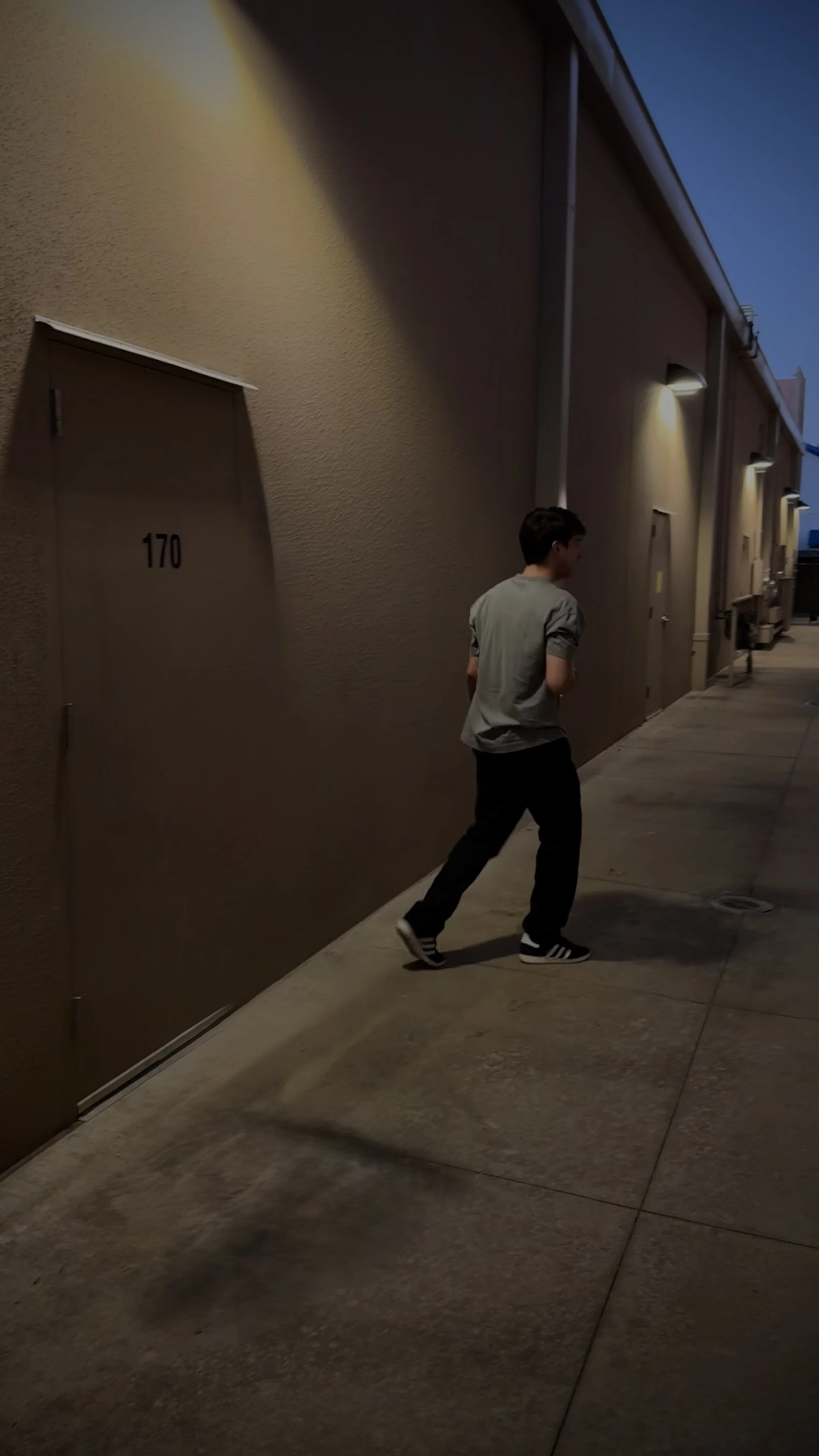 Person walking in a dimly lit alley at night with a door marked 170 on the left wall.