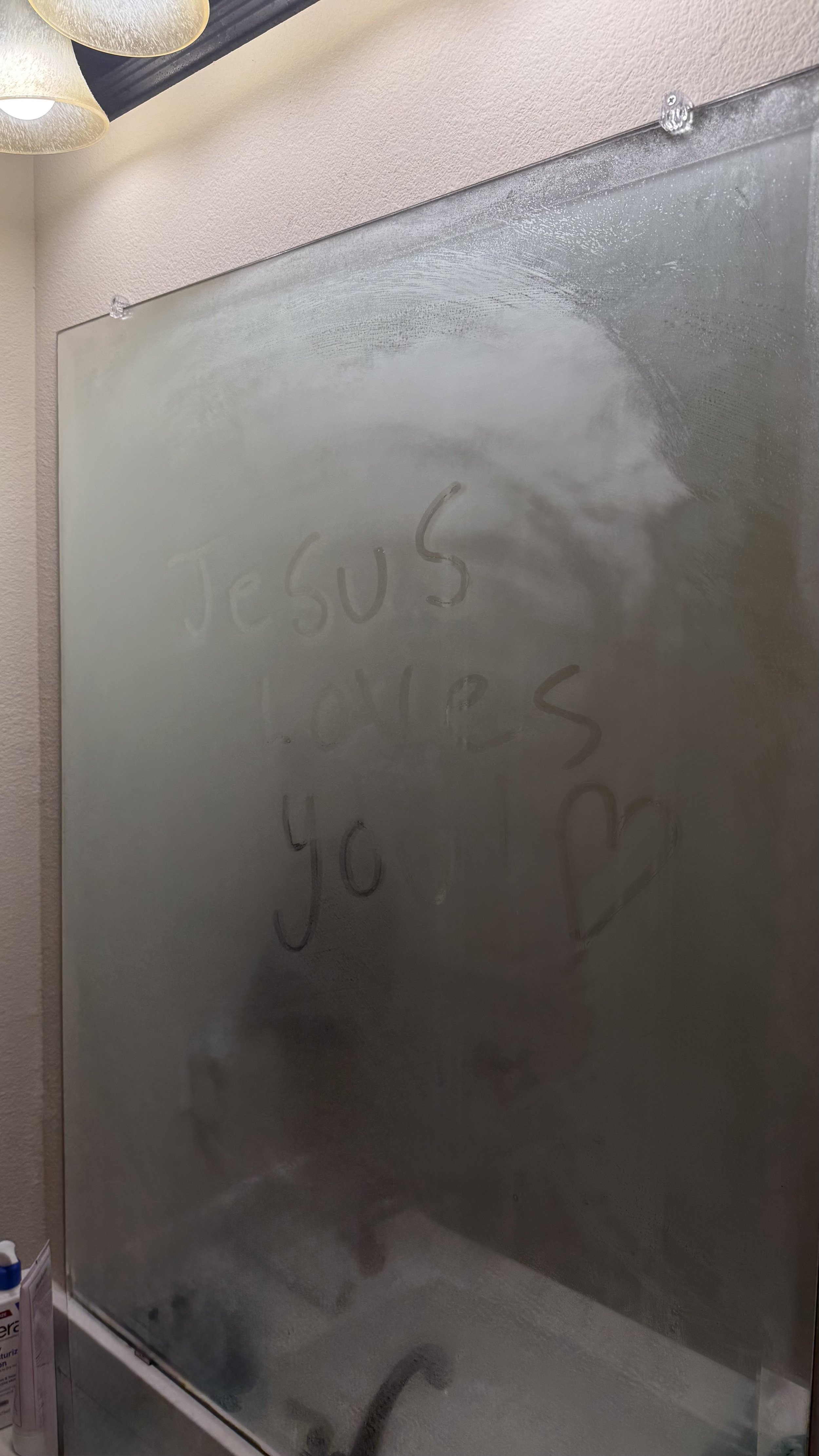 Fogged mirror with 'Jesus loves you' message and a heart drawn on it.