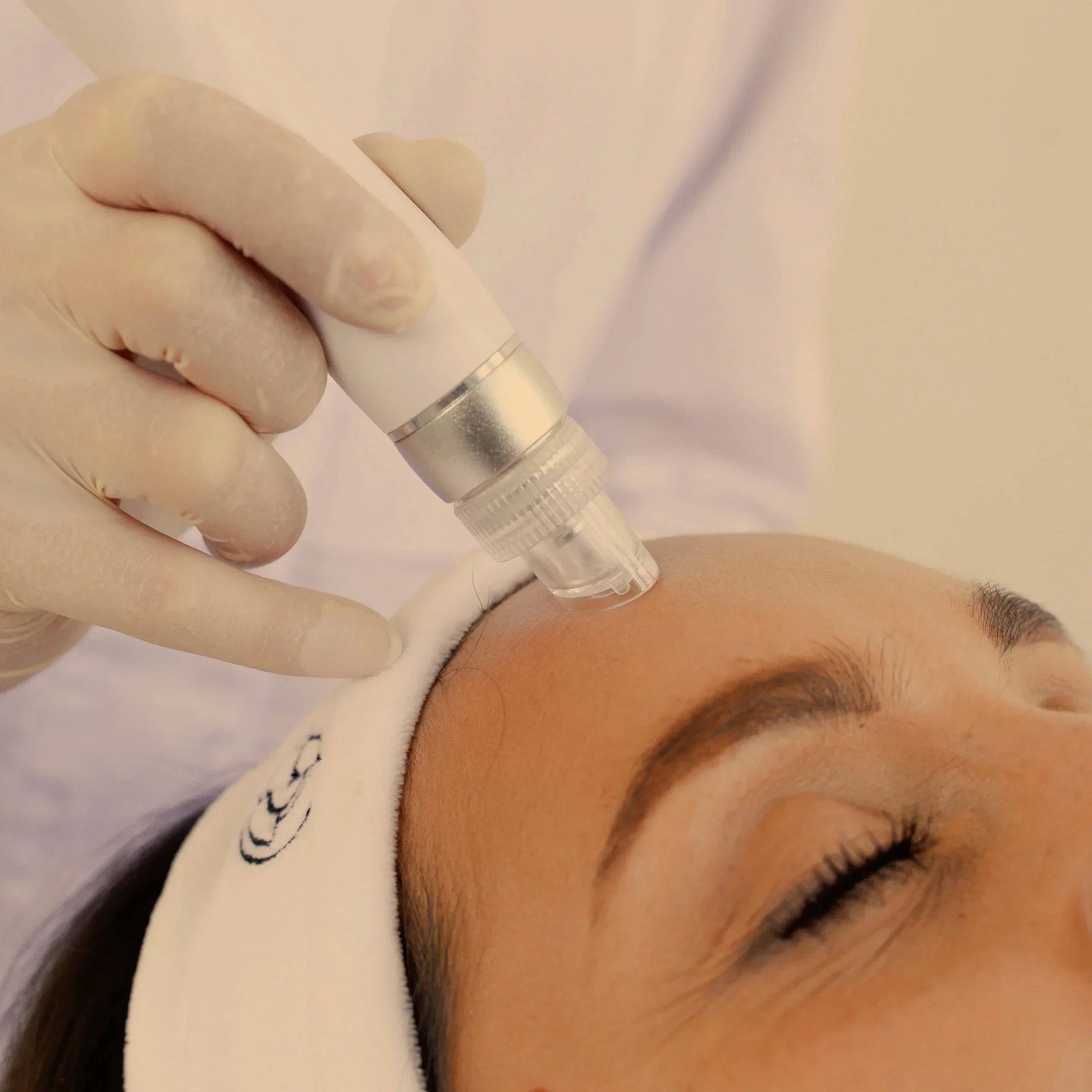 Une femme reçoit un traitement esthétique du visage à l'aide d'un appareil dans un centre médical ou spa, sous la supervision d'une spécialiste en gants blancs.