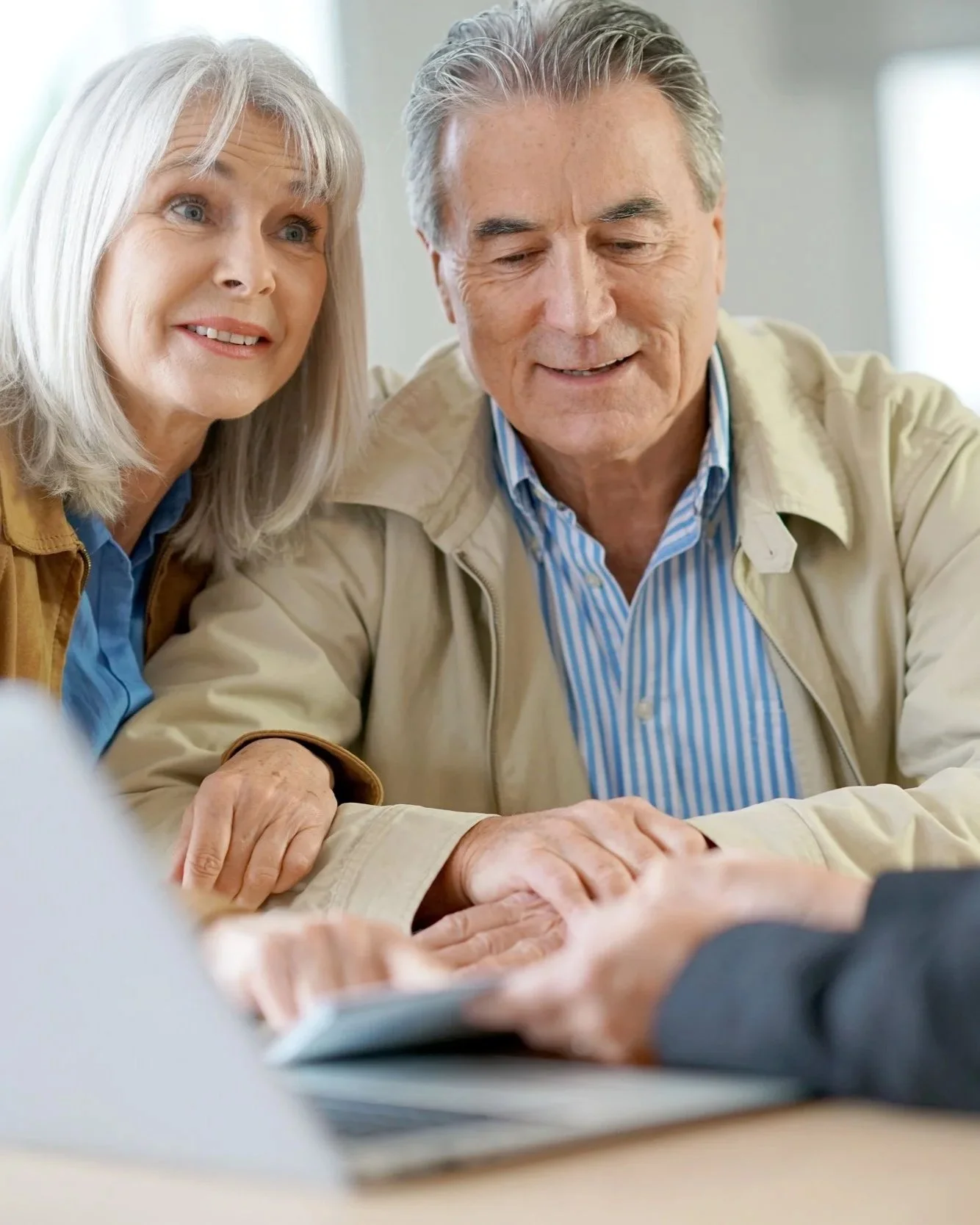 An elderly couple looking at a document with a person, possibly a financial advisor or doctor, sitting across from them.