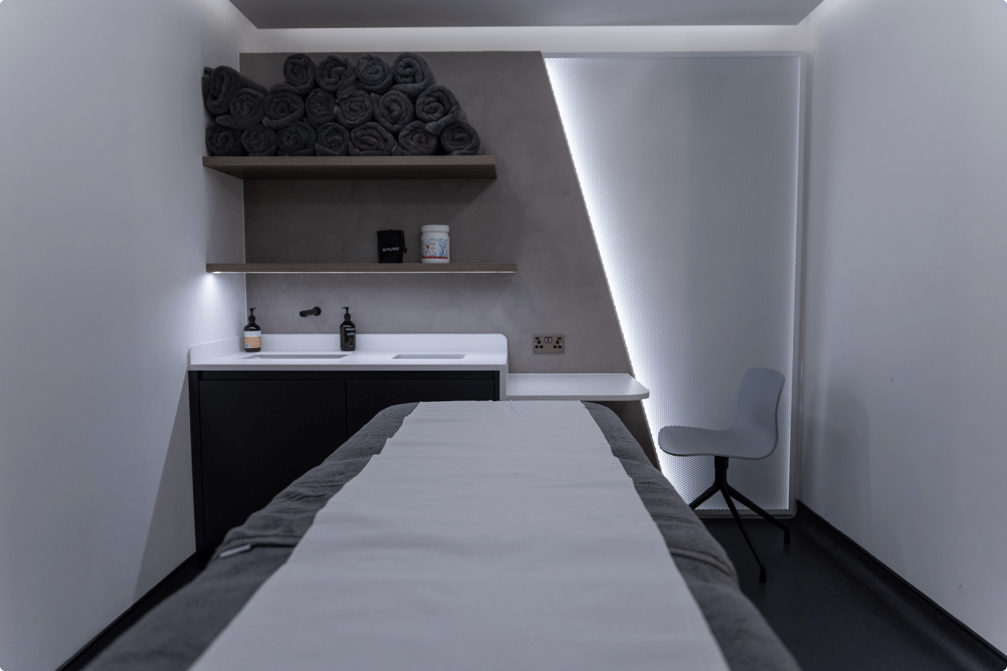Modern minimalist spa treatment room with massage table and gray towels.