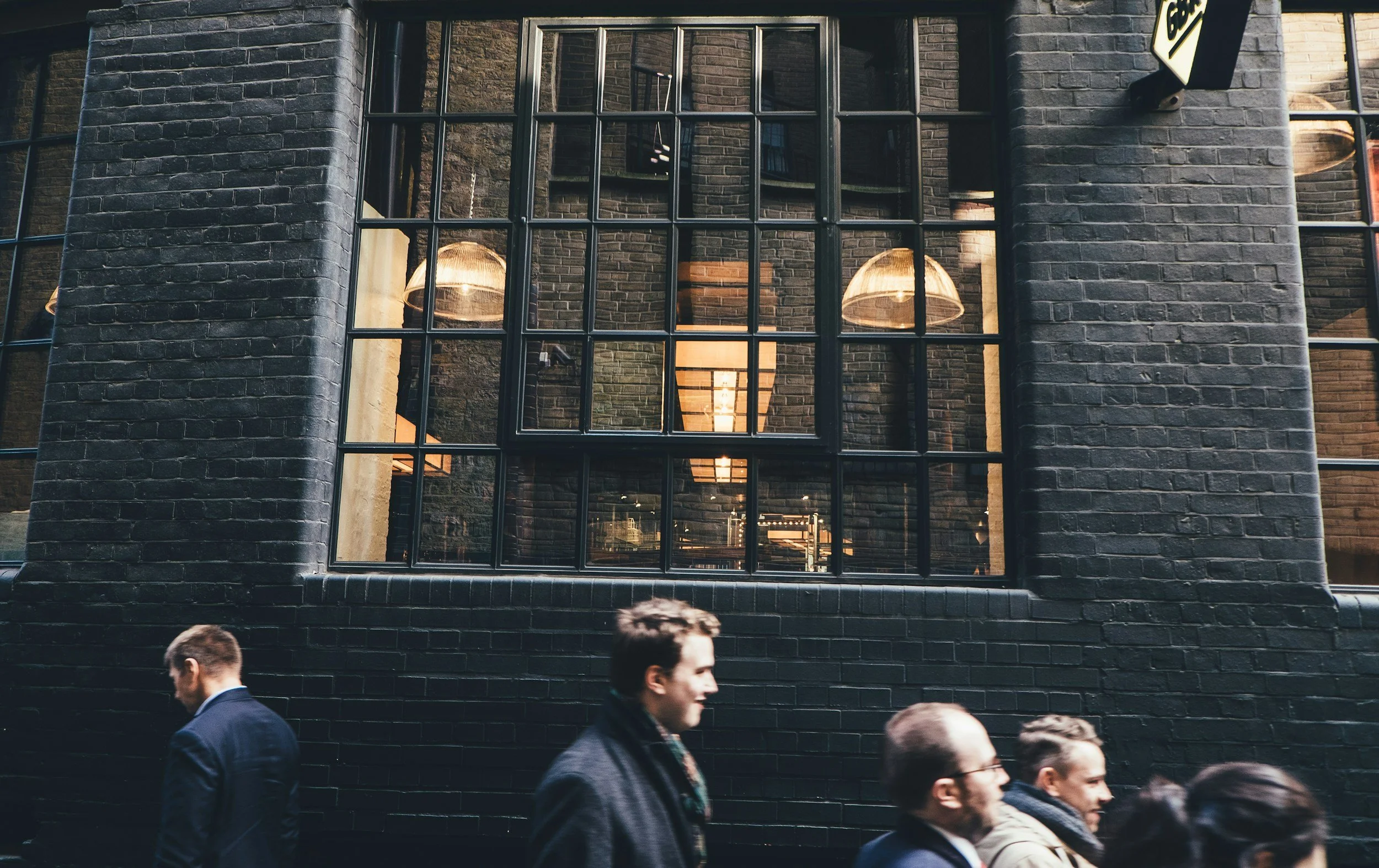 Group of people walking by a brick building with large windows