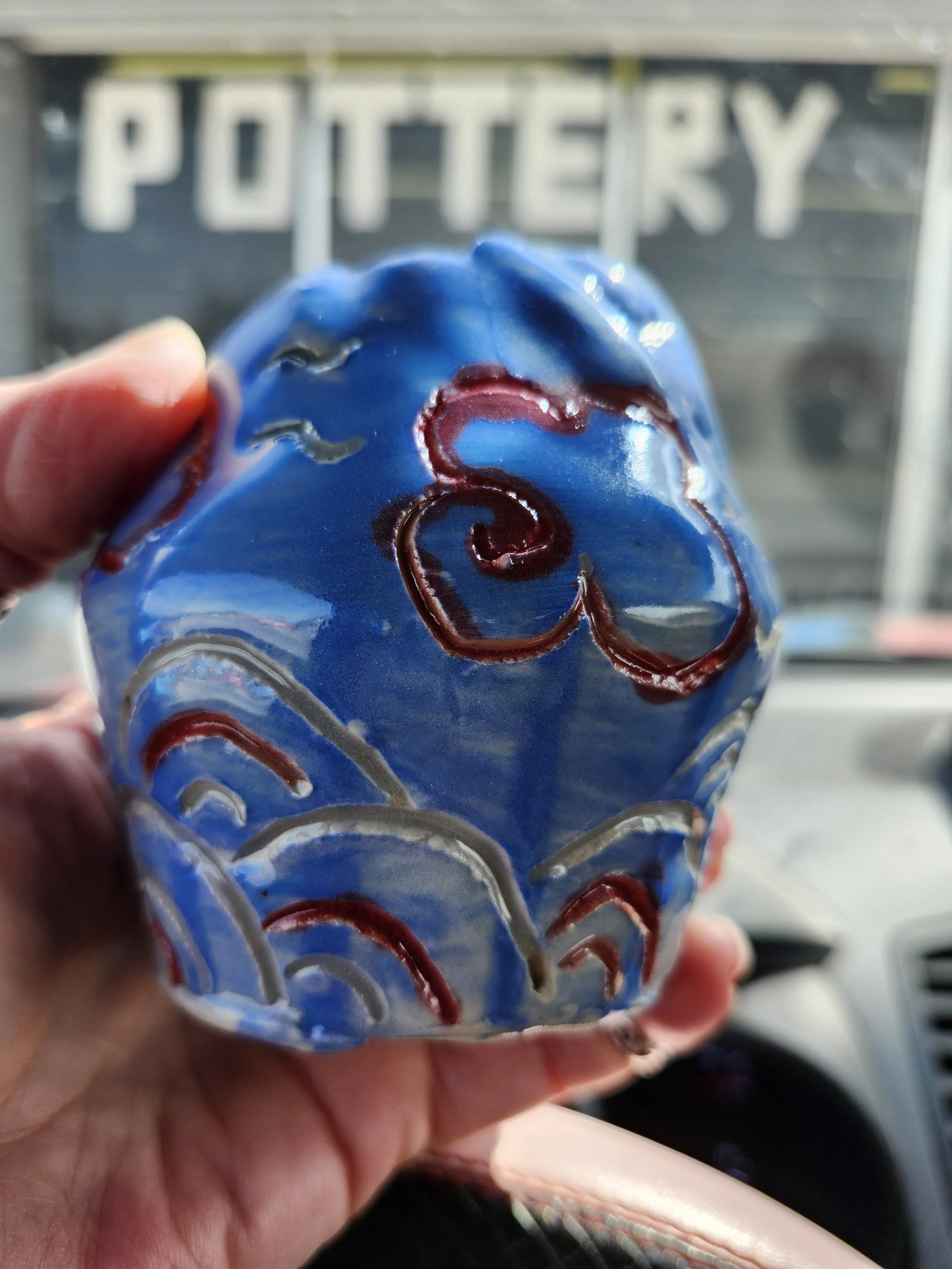 Hand Holding a glossy blue cup with red carved swirl design