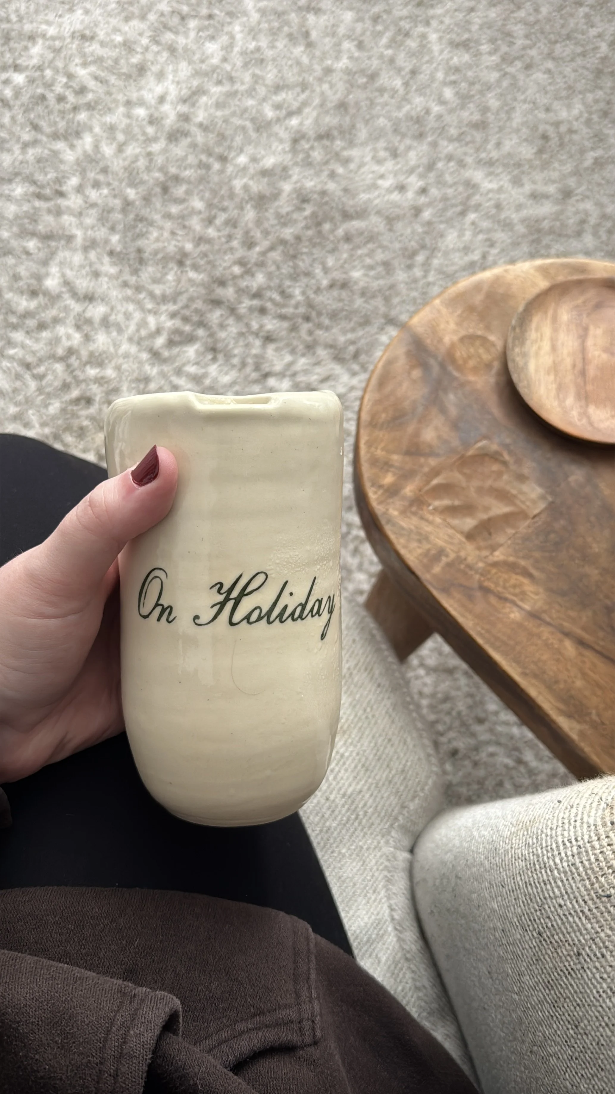 Hand holding an off-white ceramic travel mug with "On Holiday" glazed on the side