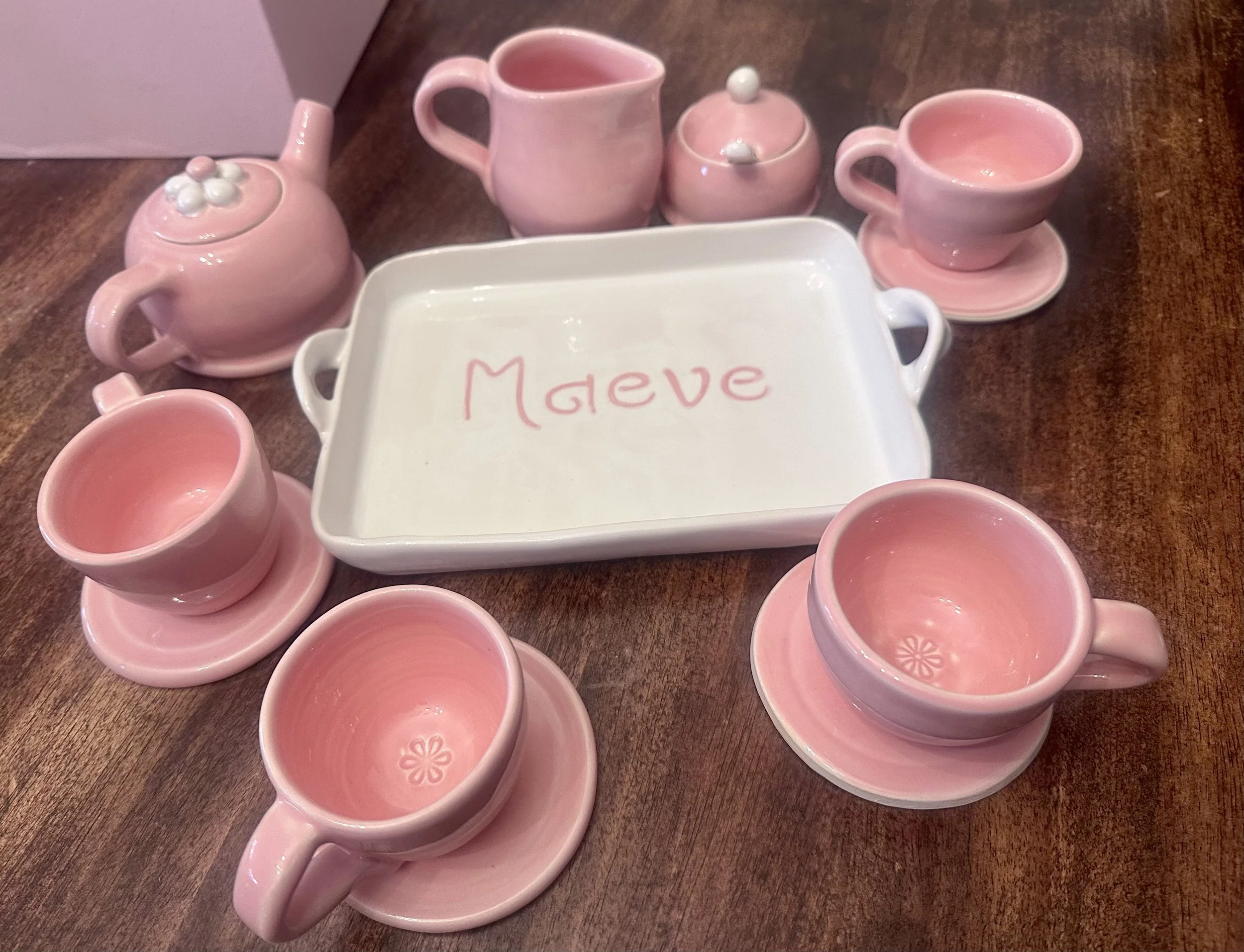 a ceramic tea set and tray in pink and white glaze with "maeve" on the tray