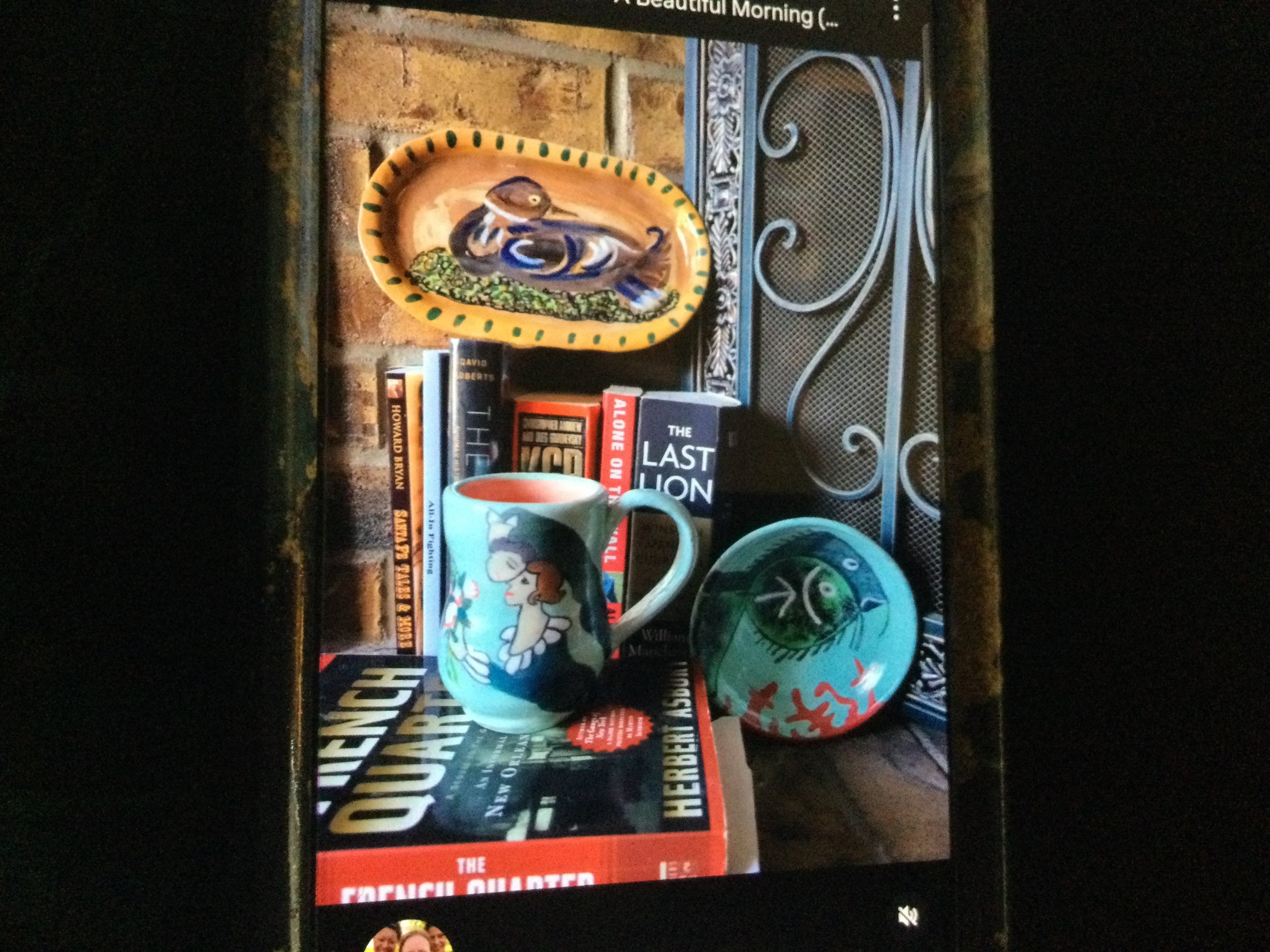 A set up of highly decorated colorful ceramic mug, plate and platter among books and a fire grate