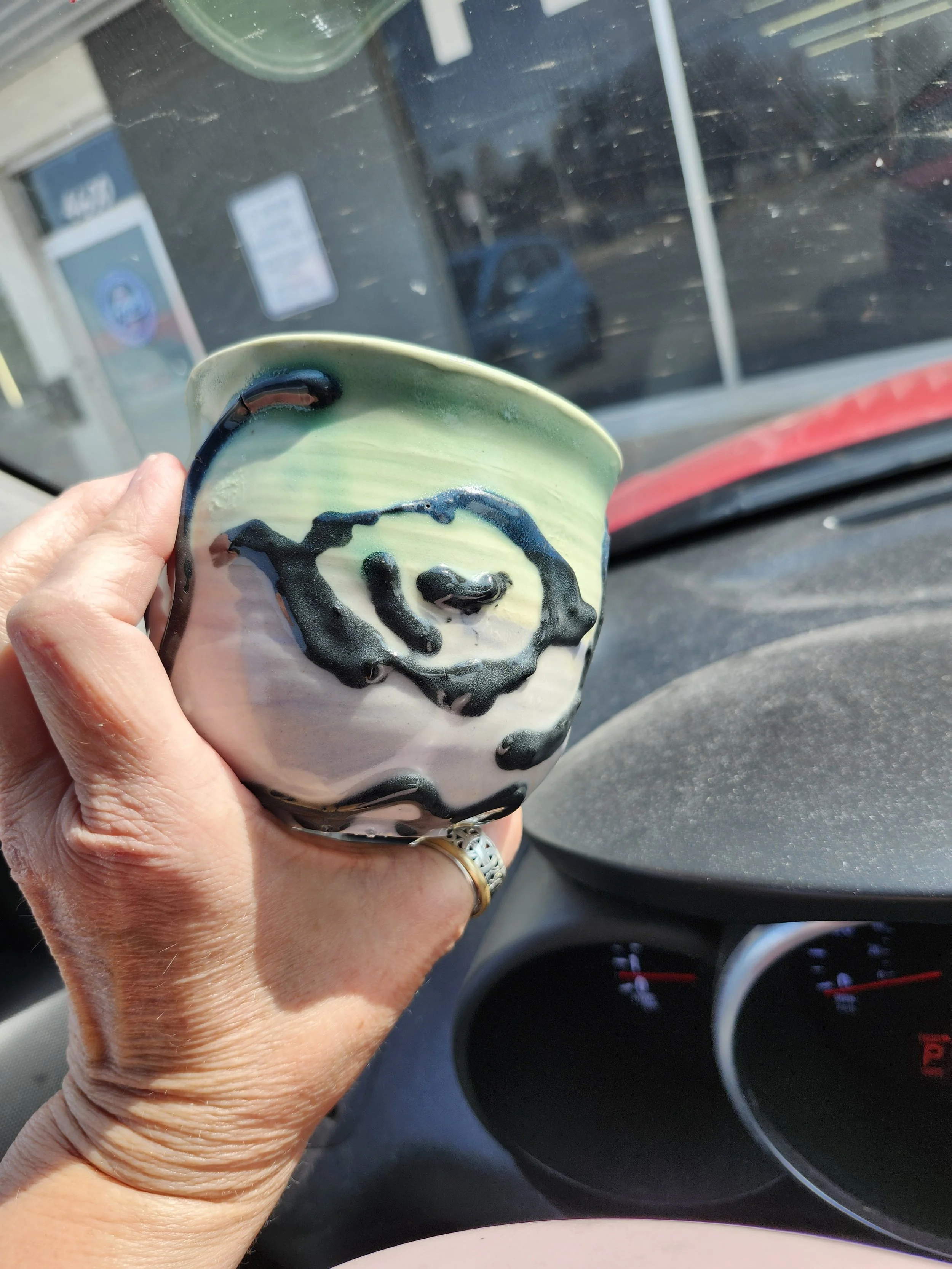 Hand holding a soft green and pink cup with black gloss swirl design