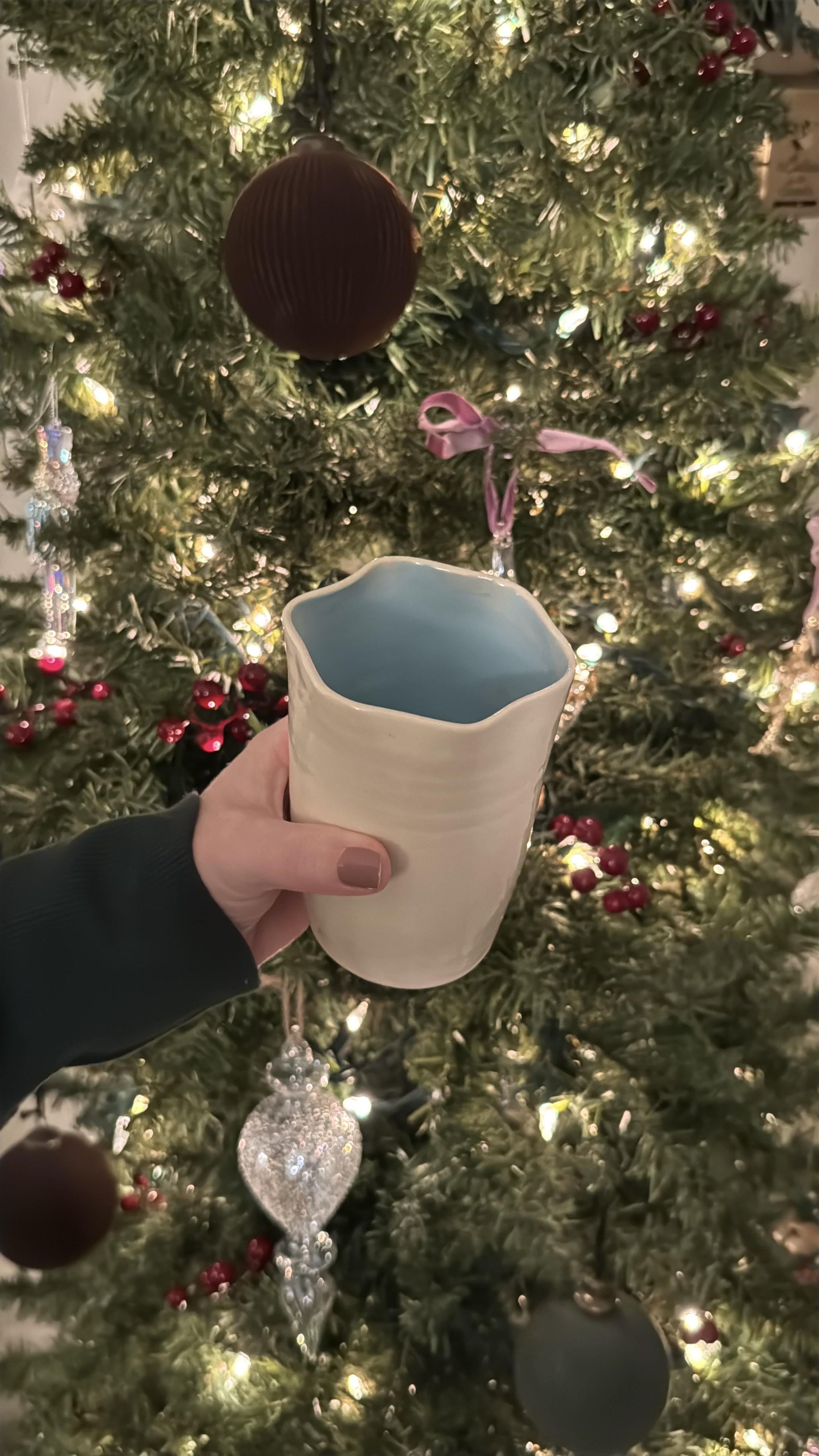 Hand holding an off-white ceramic mug with uneven rim edges and blue glaze inside