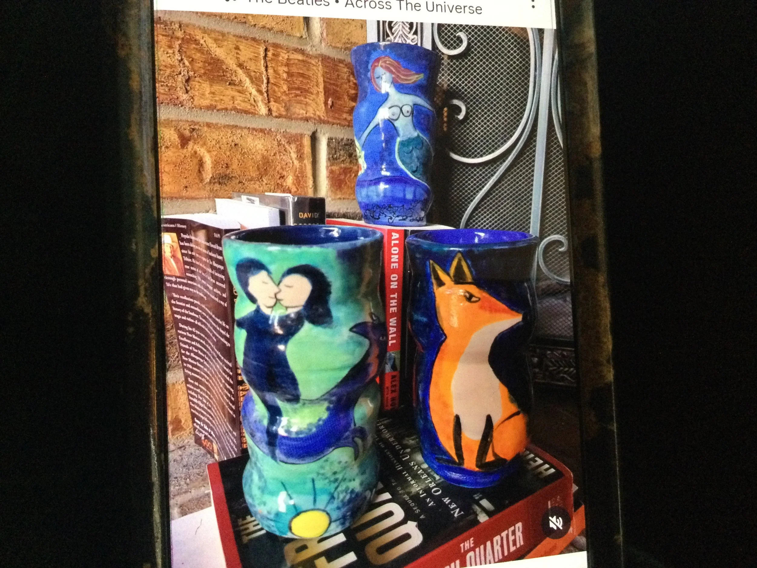 Three multi-colored illustrative ceramic vessels