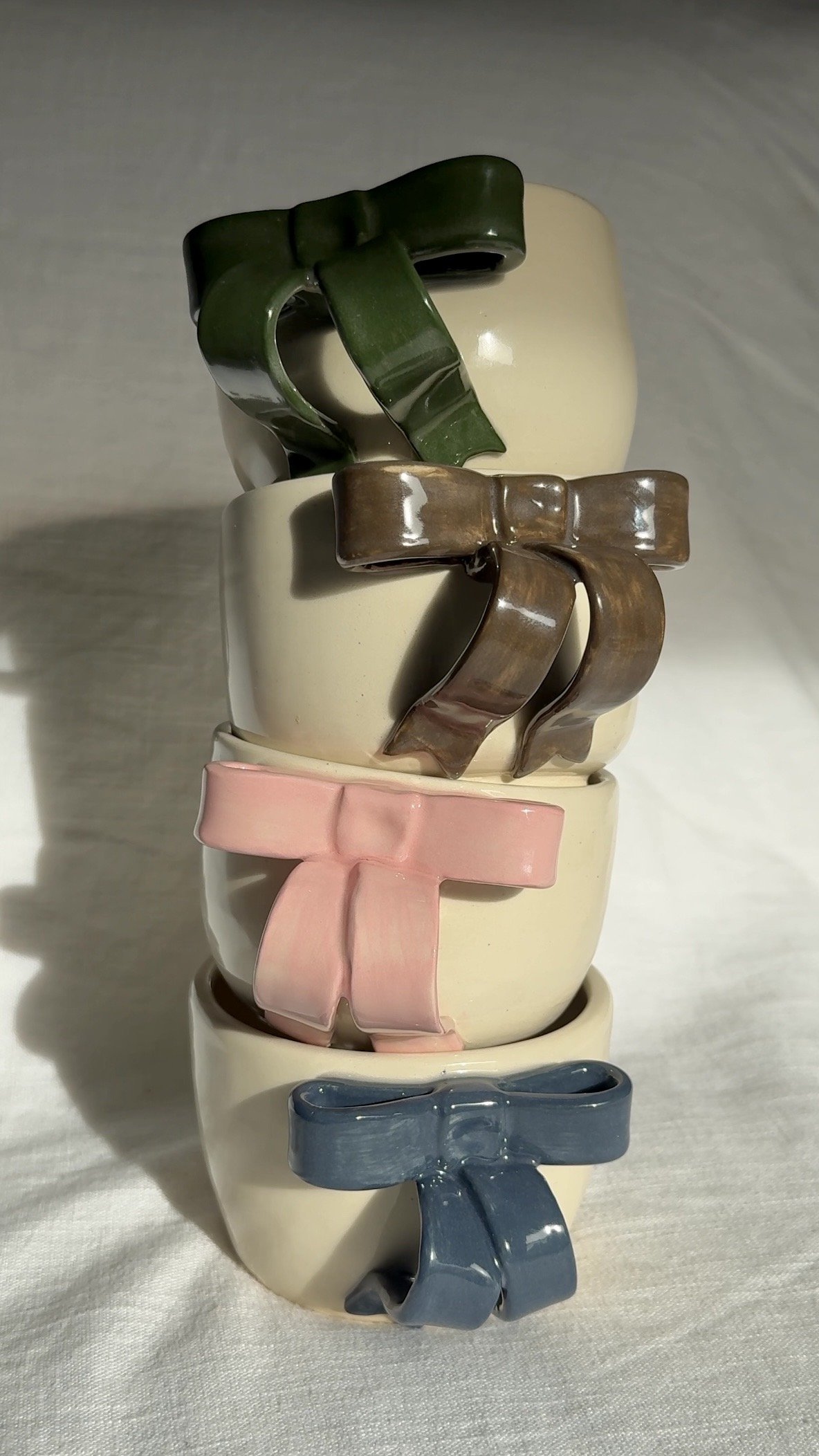 Stack of 4 ceramic mugs with 3-d bows in green brown, pink and blue
