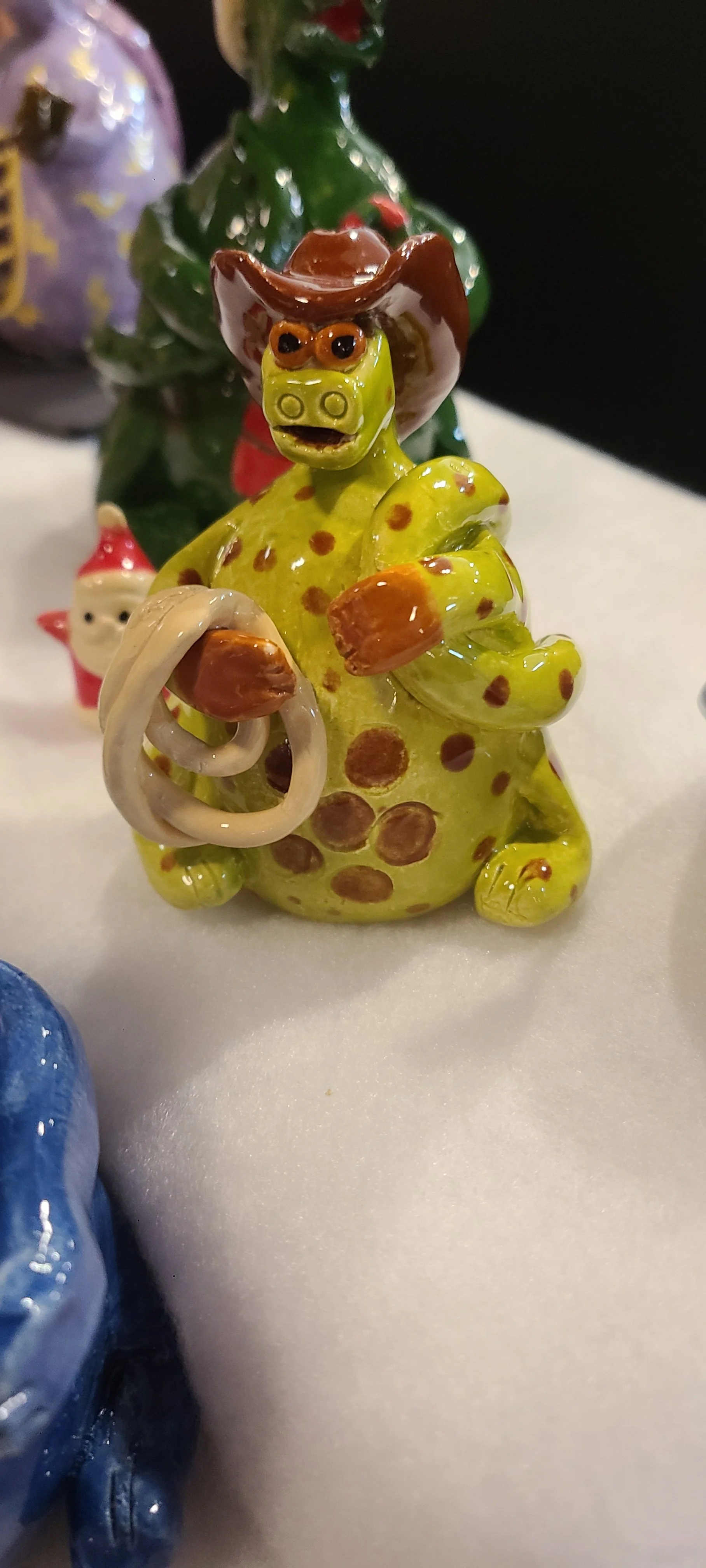 Green and brown spotted creature with cowboy hat and rope