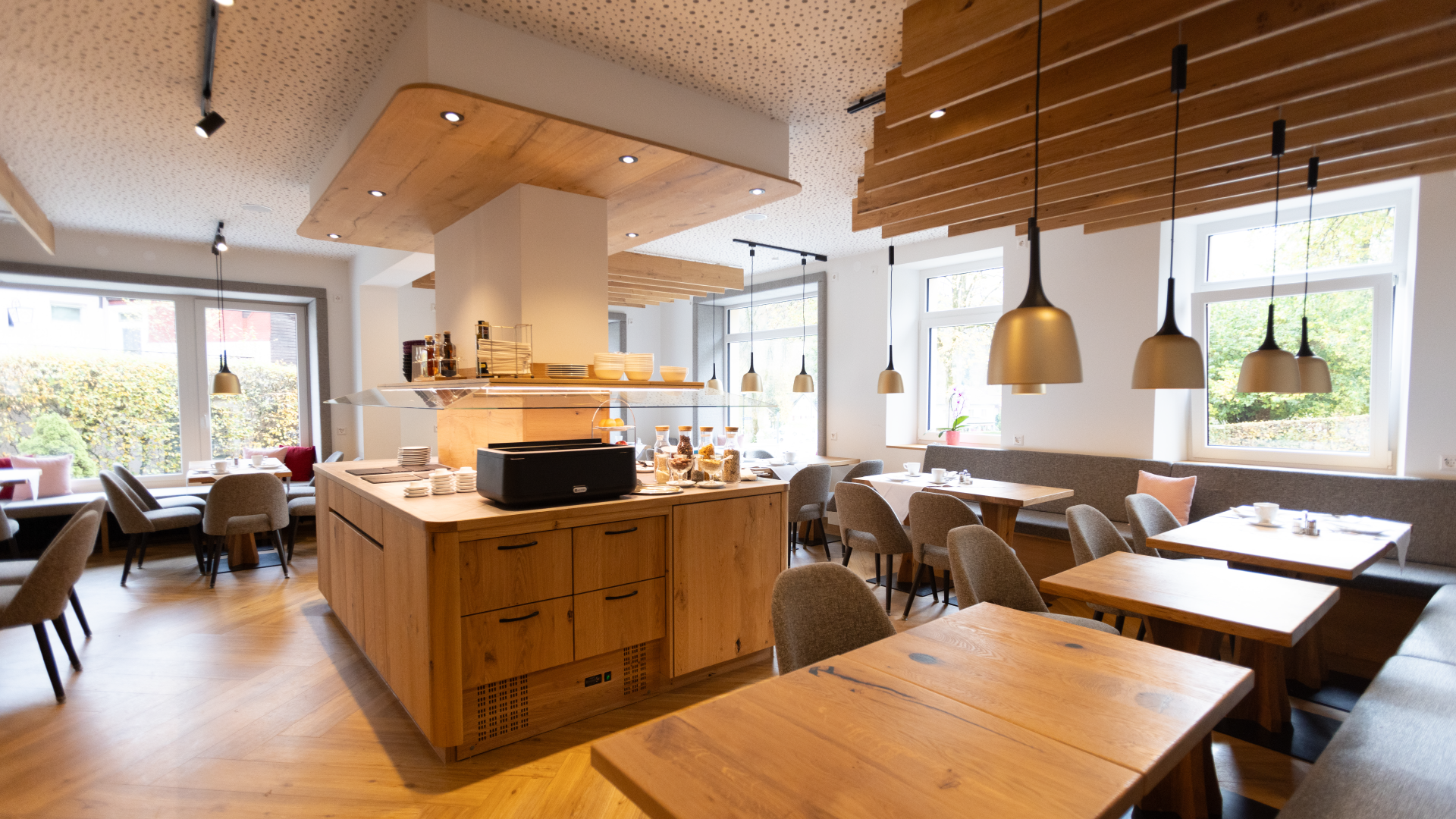 Gemütliches, modern eingerichtetes Café mit Holztischmöbeln, großen Fenstern und hängenden Lampen