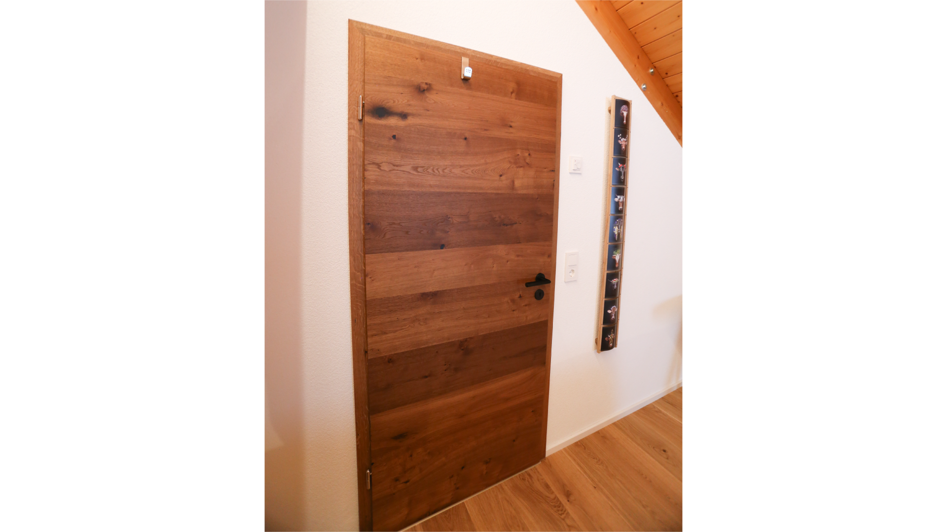 Holztür in einer weißen Wand in einem Raum mit Holzfußboden und einer vertikalen Bilderleiste an der Wand.
