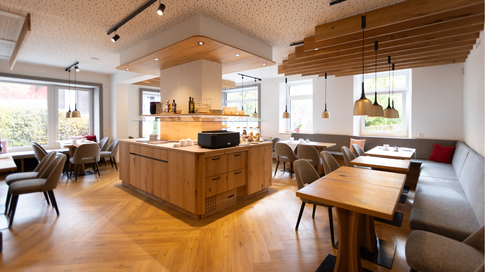 Inneneinrichtung eines Restaurants mit Holztischen, Stühlen und großen Fenstern für natürliches Licht.