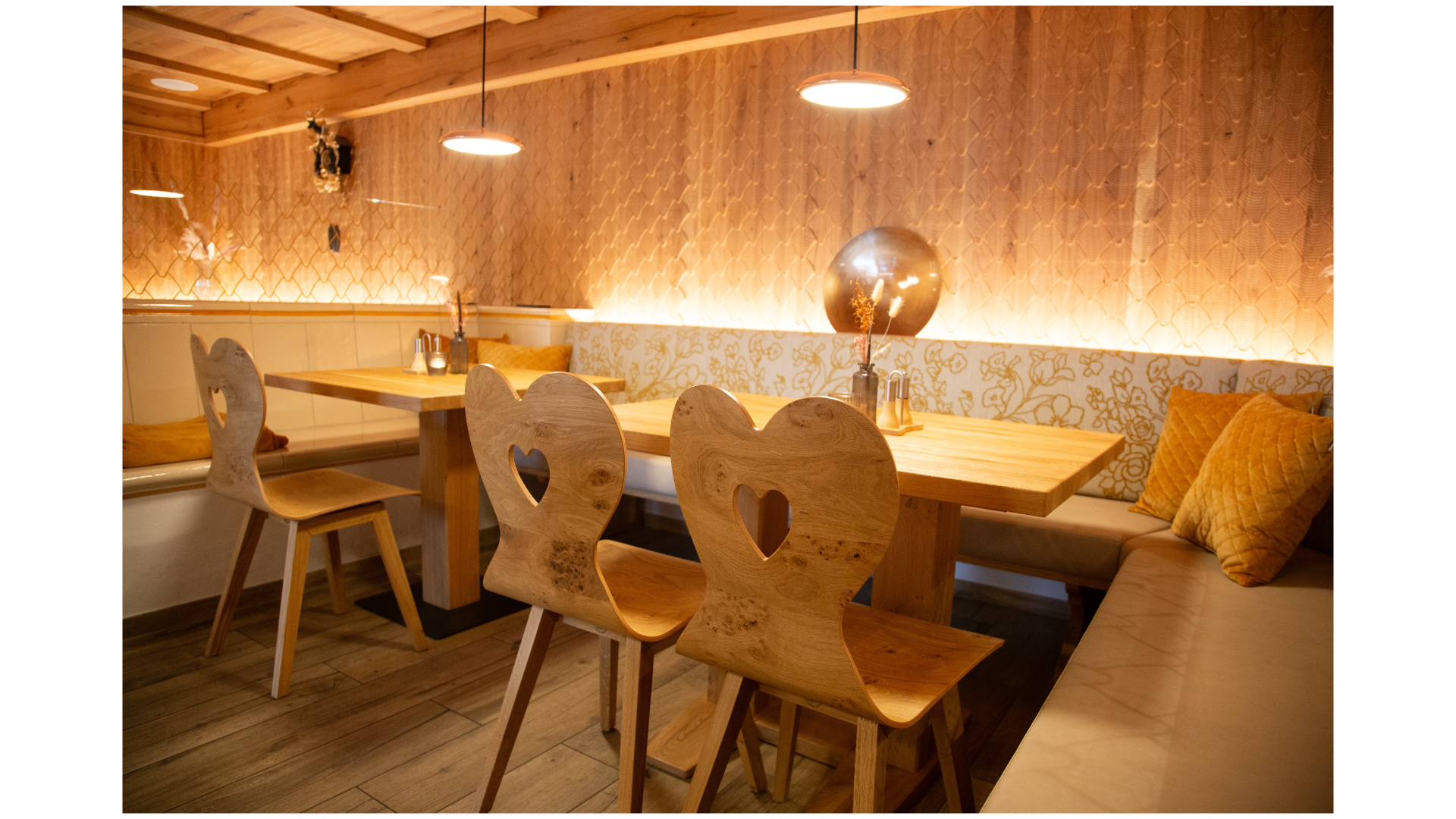 Gemütliches Restaurant mit Holzstühlen, Sitzbänken, warmen Beleuchtung und golden Dekorationen.