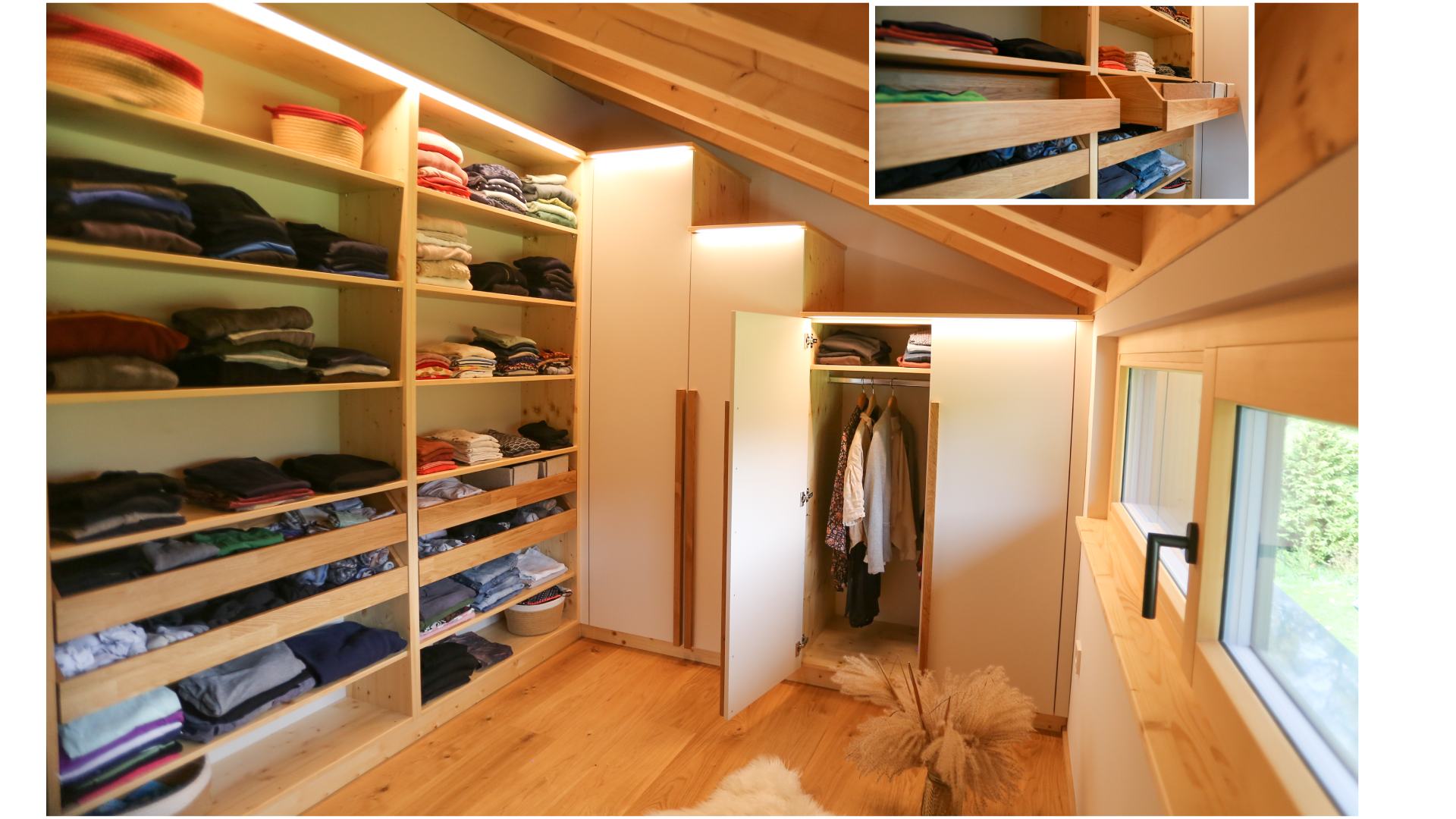 Ein Schlafzimmer mit Holzregalen, voll mit gefalteter Kleidung, und einem offenen Schrank mit hängender Kleidung. Es gibt einen Dachboden mit Sichtfenster und natürlichem Licht sowie eine Vase mit getrockneten Pflanzen auf dem Boden.