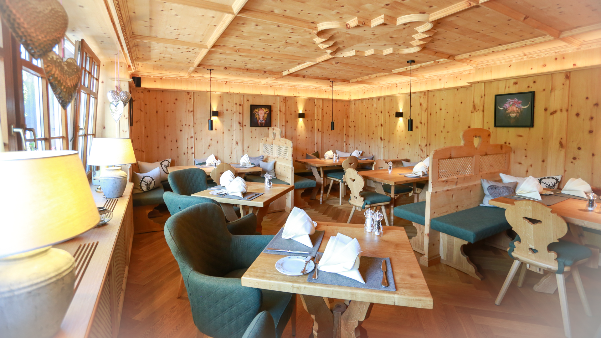 Gemütliches Restaurant mit Holzmöbeln, Tischen mit weißen Stoffservietten und Besteck, stilvolle Beleuchtung und Wanddekorationen im Holzdesign.