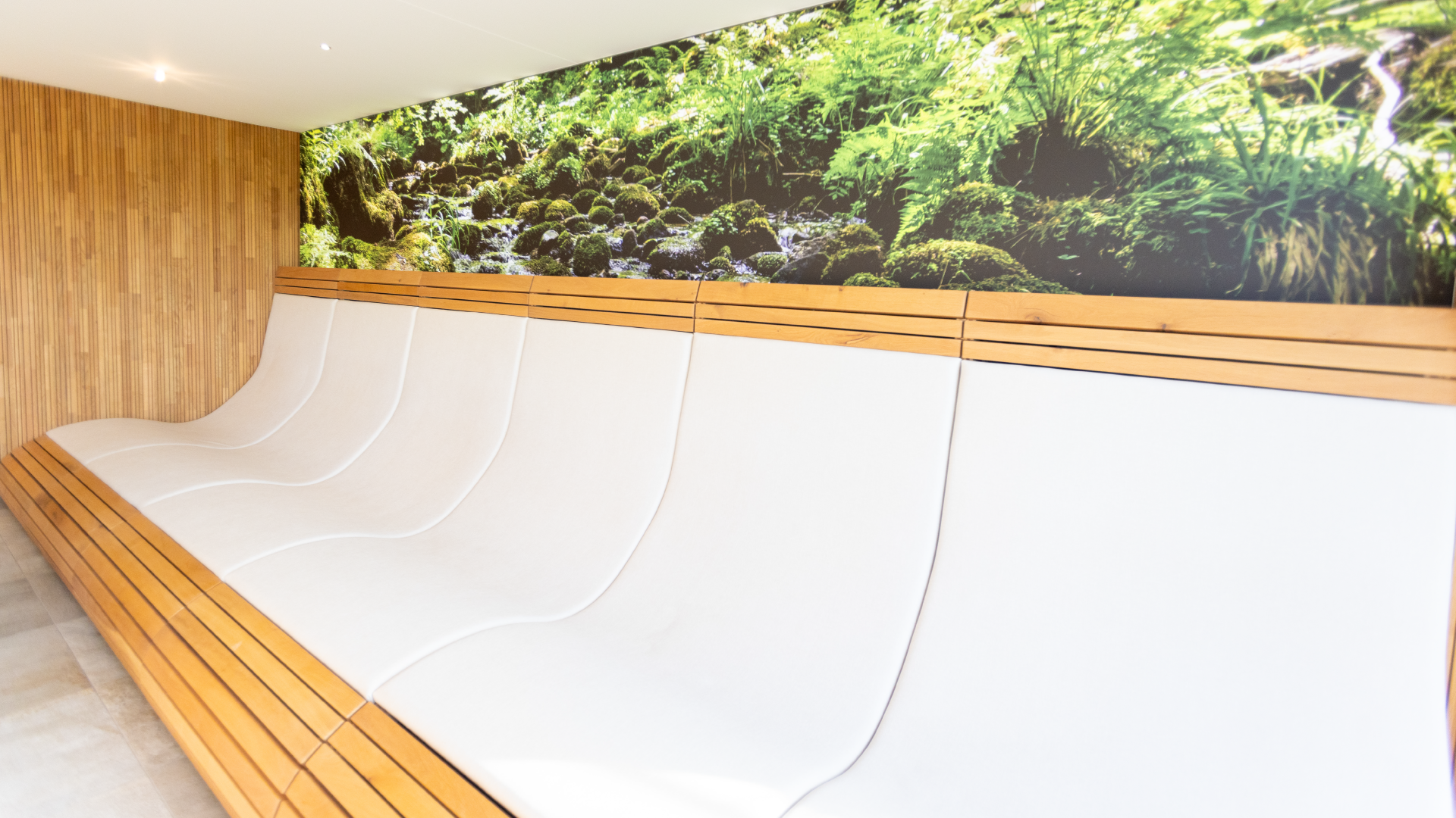 Wartebereich mit weißem Sitzbank und Holzverkleidung an der Wand, großes Wandbild einer Waldlandschaft mit Moosen und Wasser