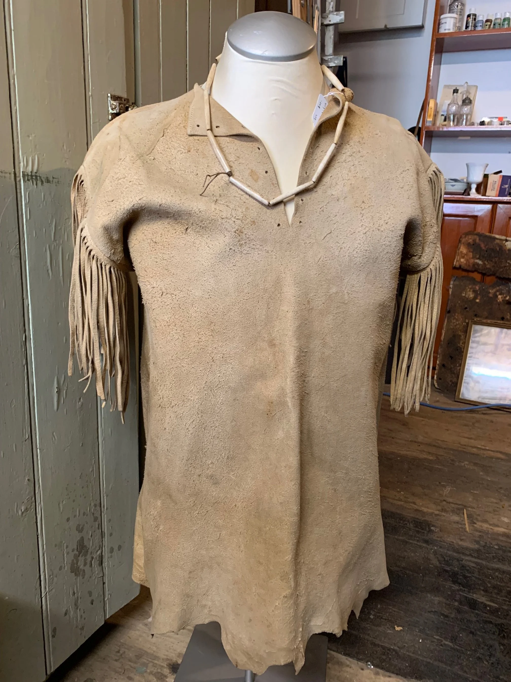 Beige suede Indigenous tunic with fringes on the sleeves displayed on a mannequin.