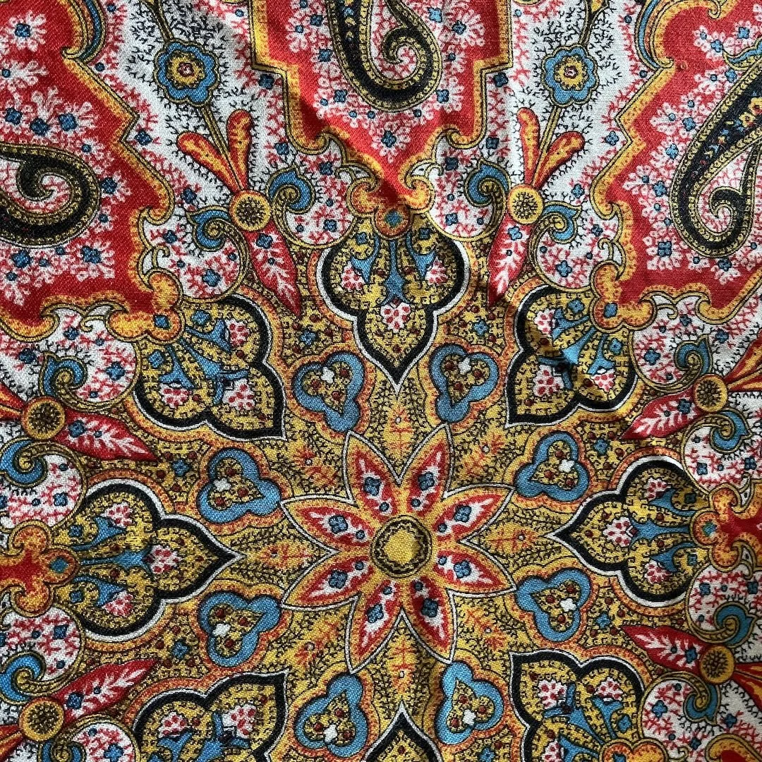 Close-up image of a colorful, intricate paisley pattern with red, yellow, blue, black, and white details.