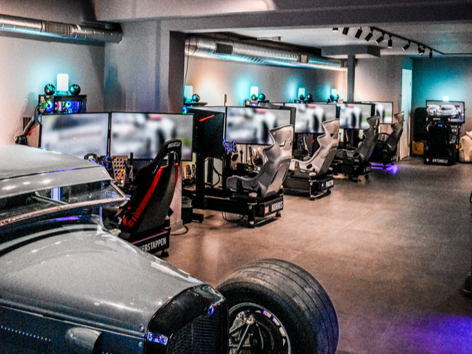 Two people in racing simulators, wearing headphones, playing a driving video game on curved monitors.