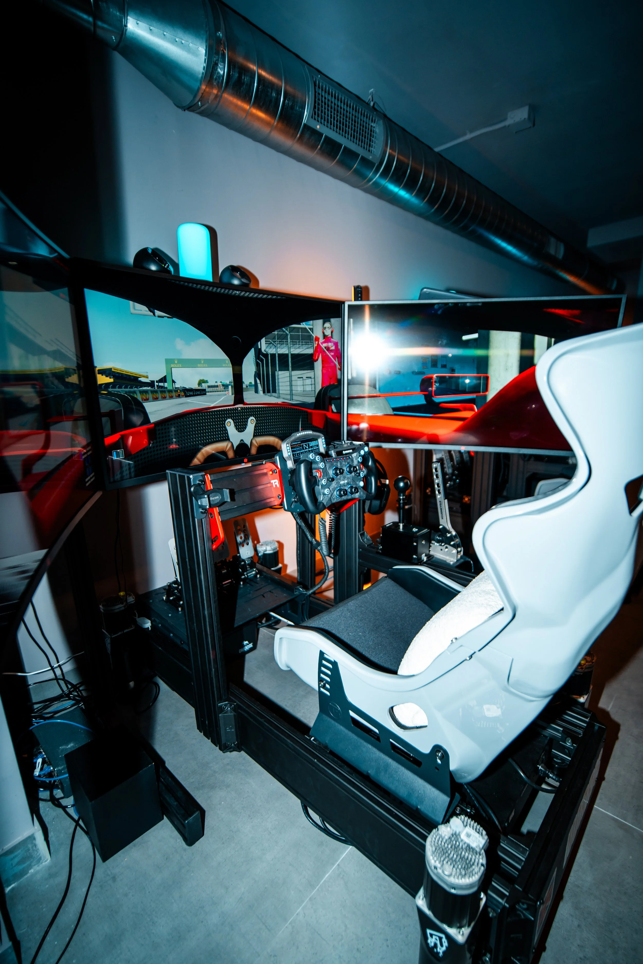 Person playing a racing simulator with a steering wheel and multiple monitors showing a racetrack.